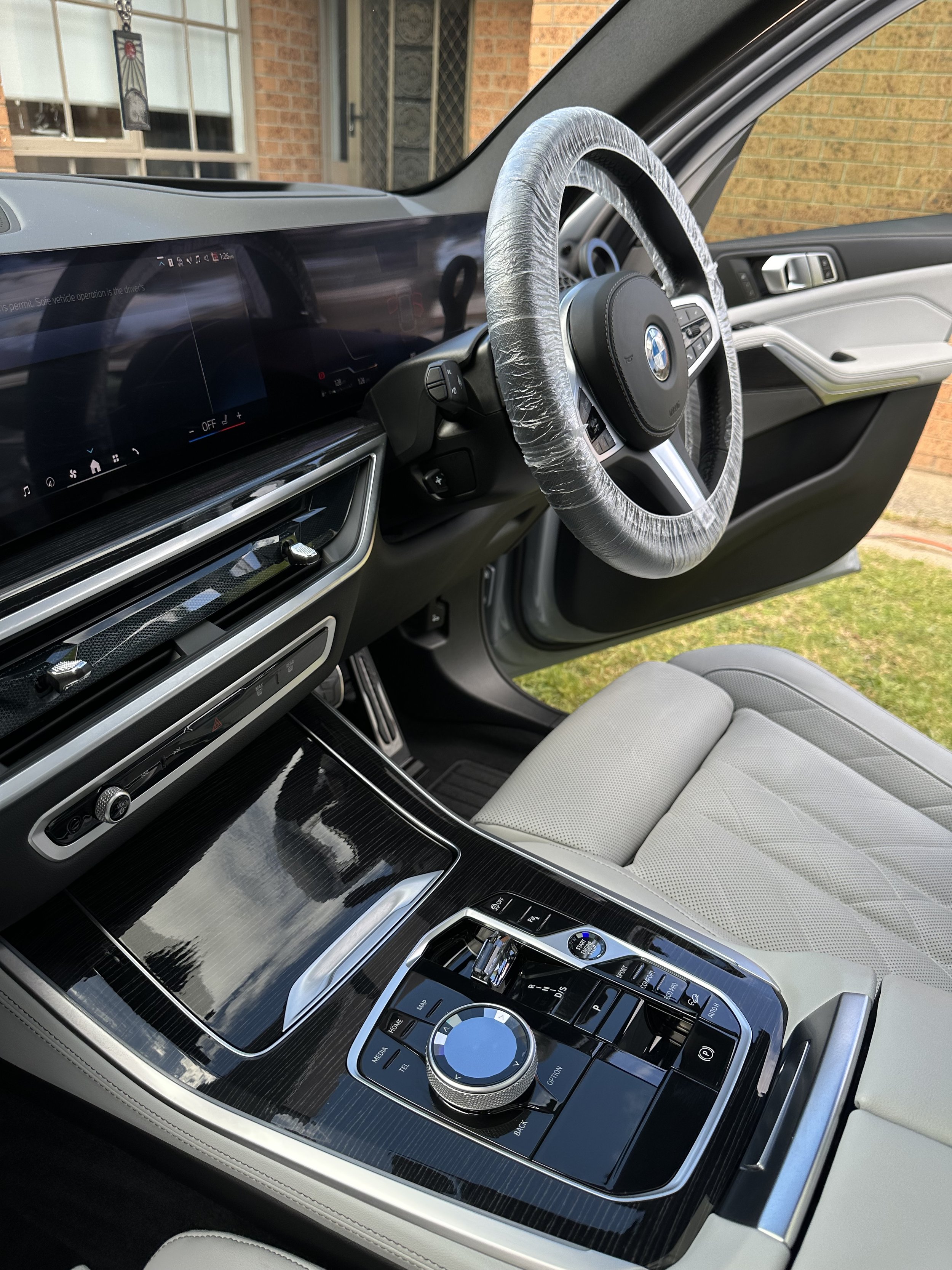 Interior of a BMW vehicle showing the steering wheel, digital dashboard, and center console with controls and a rotary dial.