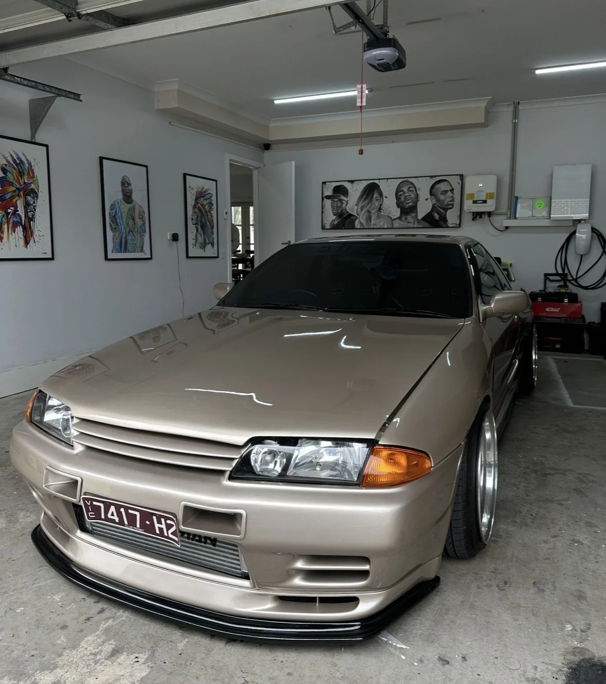 A beige sports car with a lowered body kit parked inside a garage with art on the walls.
