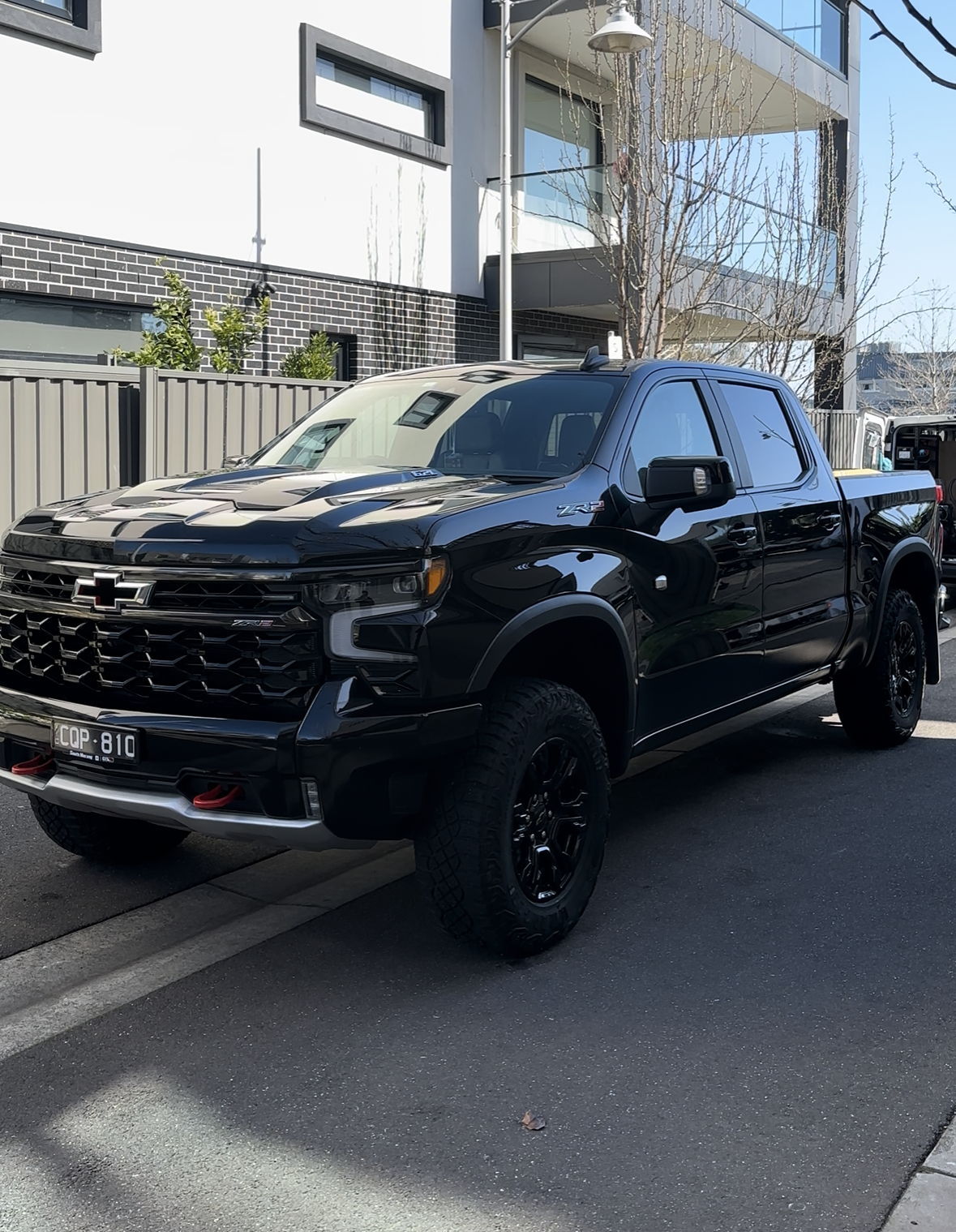 A black Chevrolet pickup truck parked on a city street in front of modern apartment buildings and trees.