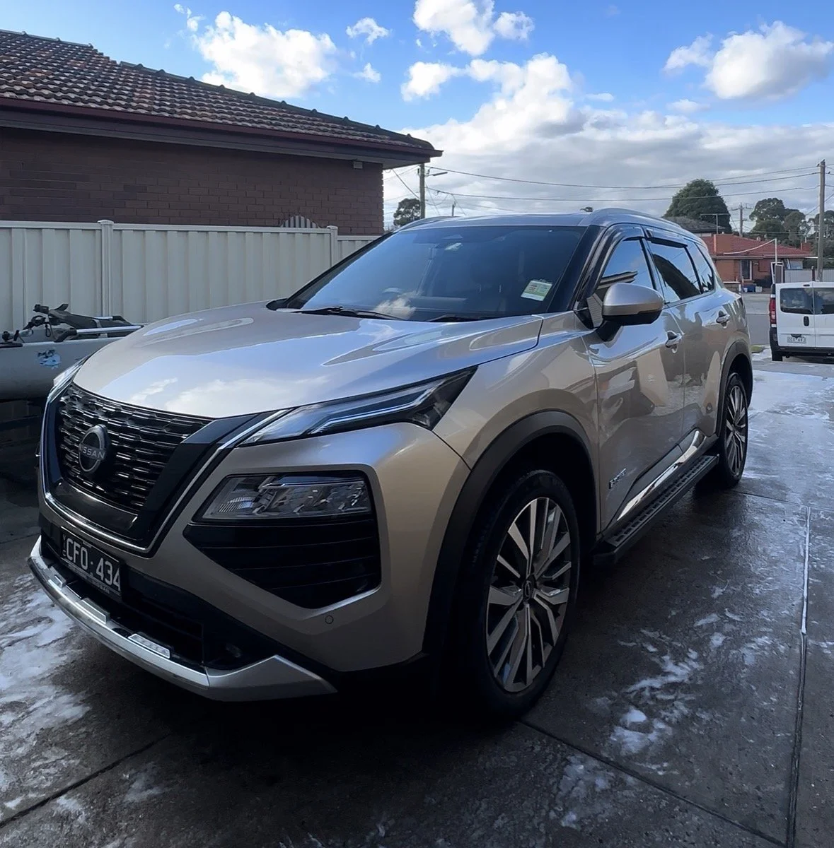 Silver Nissan SUV parked on driveway outside house with cloudy sky in background.