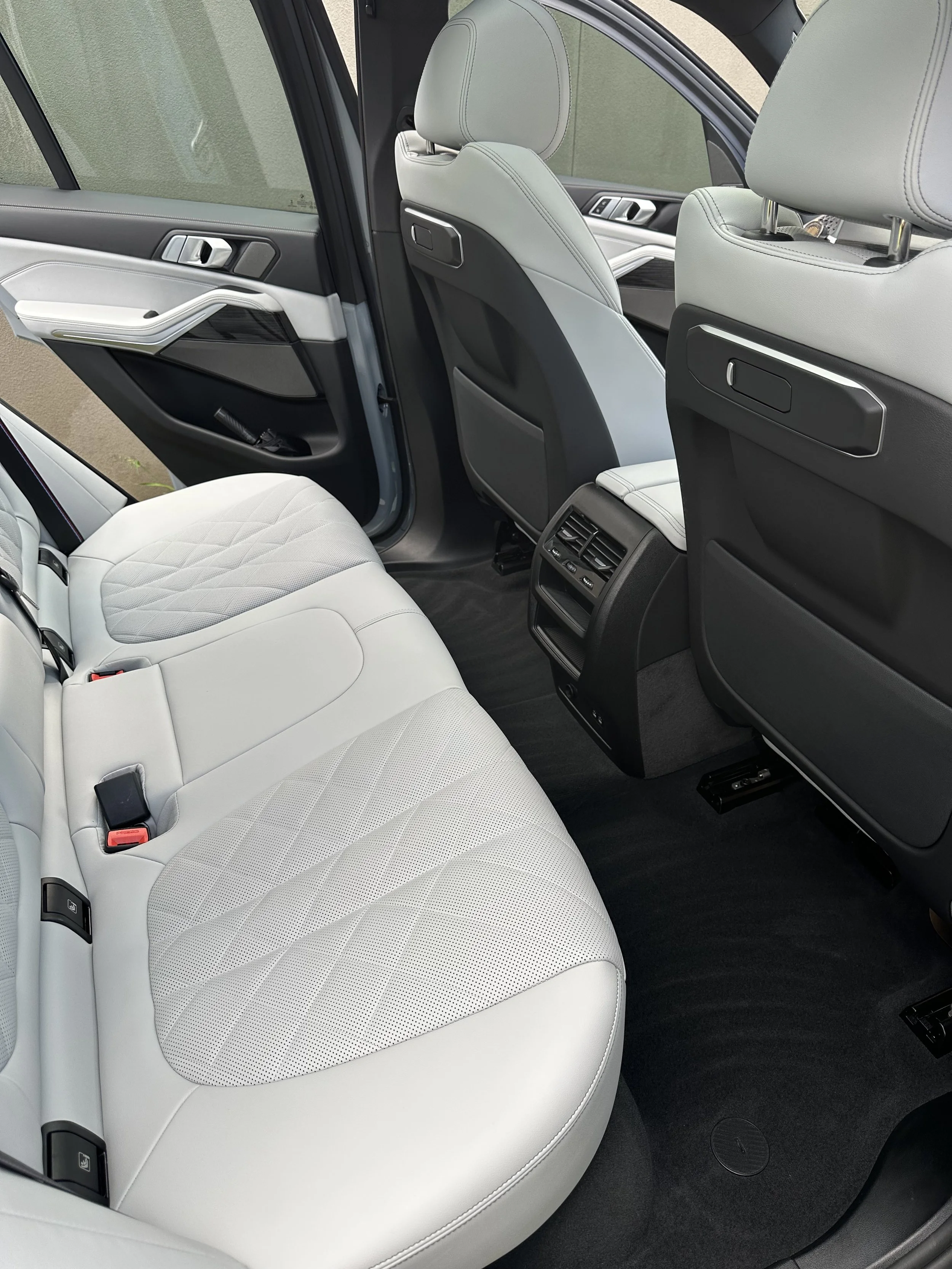 Interior of a modern car showing white leather back seats, rear air vents, and black flooring.