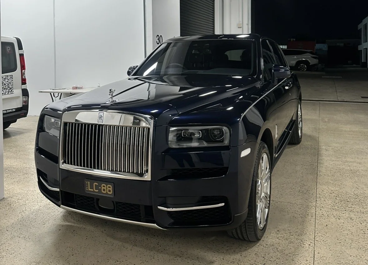 Black Rolls-Royce SUV parked indoors at night, front view.