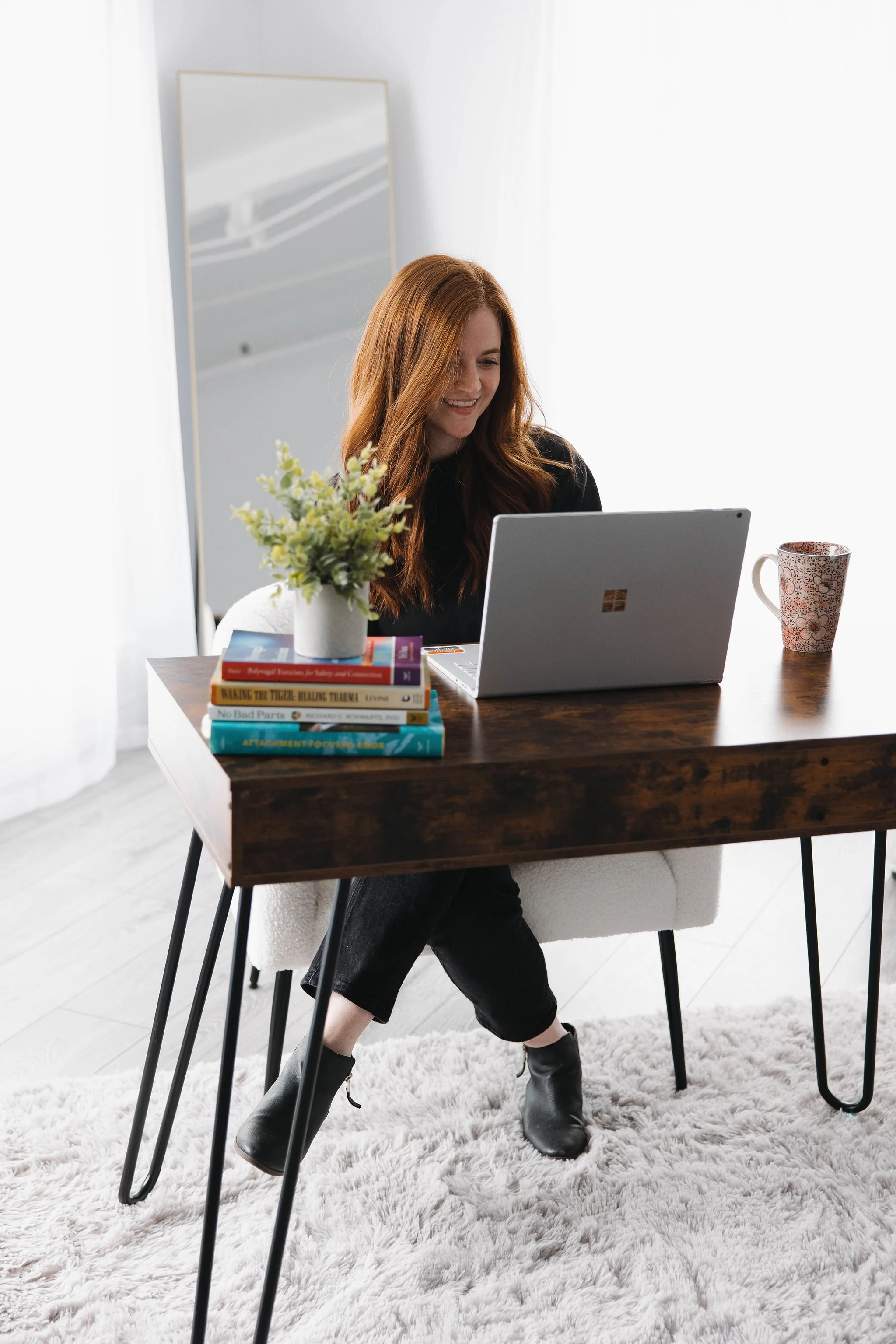 A woman sitting at a desk with a laptop and books on the desk.