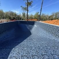 Empty swimming pool with blue tiles and surrounding trees and fencing