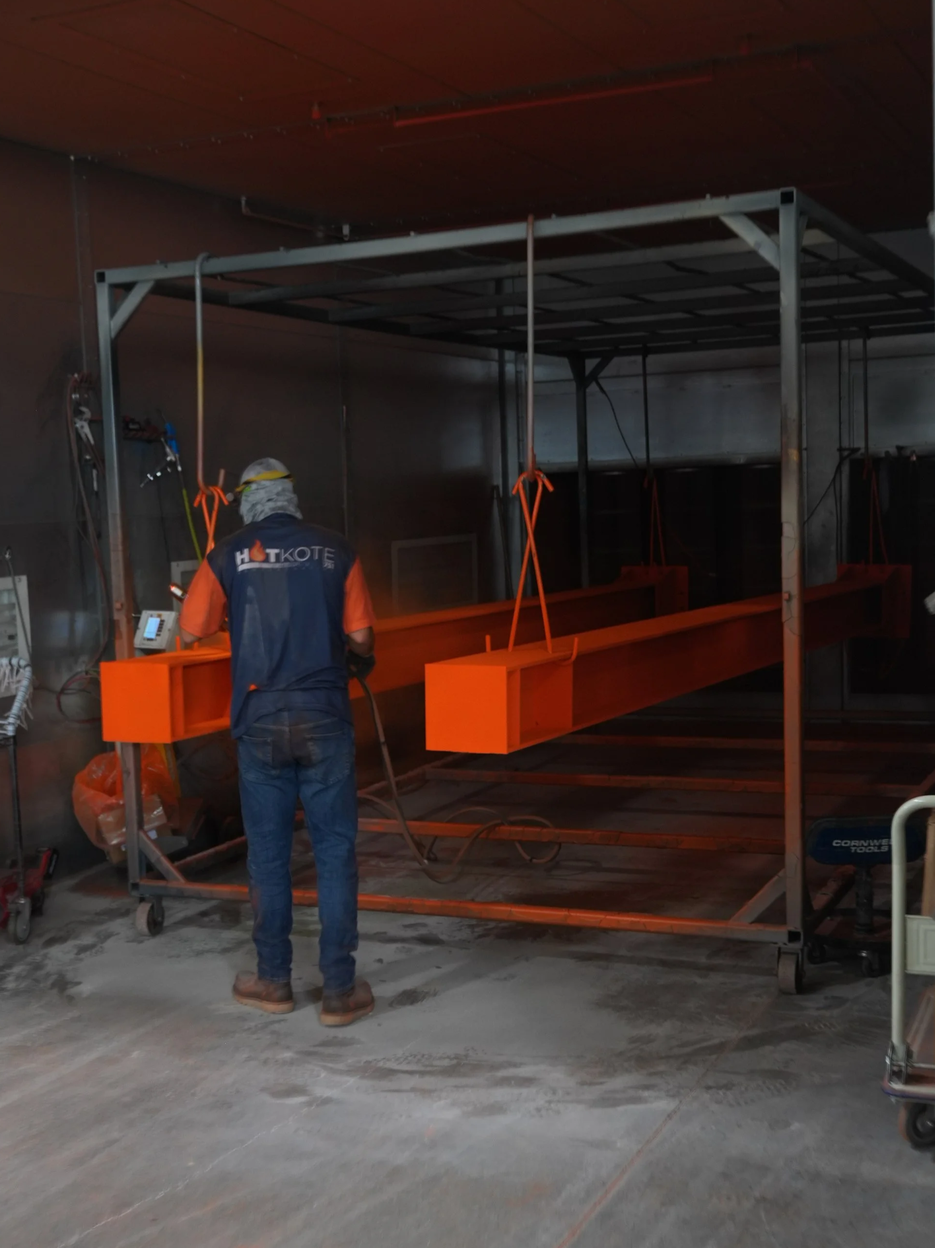 Construction worker standing on a concrete floor in an indoor construction site, working on an orange metal scaffold or structure.