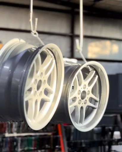 Two car wheels with white multi-spoke rims hanging from hooks in a workshop.