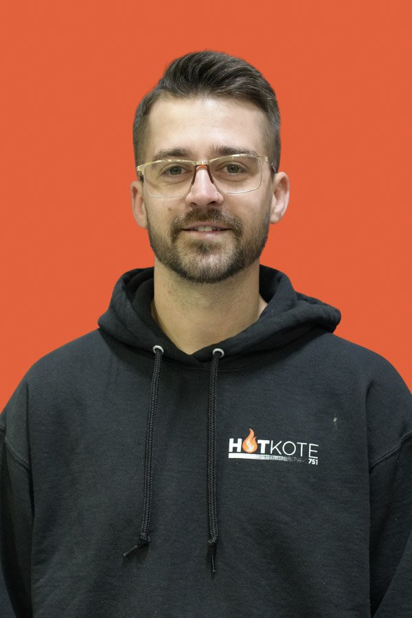 A man with glasses and a beard wearing a black hoodie with 'HOTKOTE' logo on a red background.