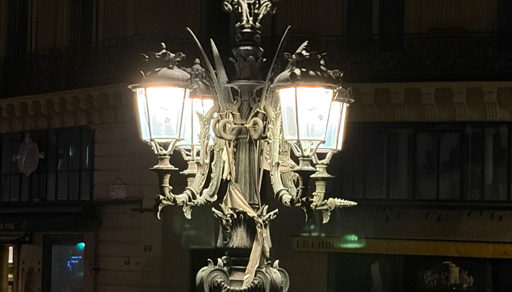 A vintage ornate street lamp with four glowing lanterns on a dark night.