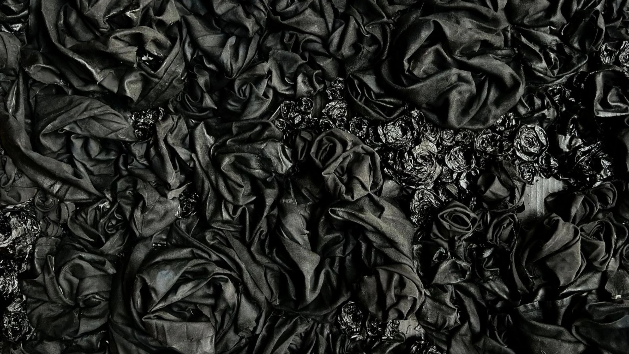 A large pile of black crumpled fabric or material, possibly sheets or clothing, with some shiny black items mixed in.