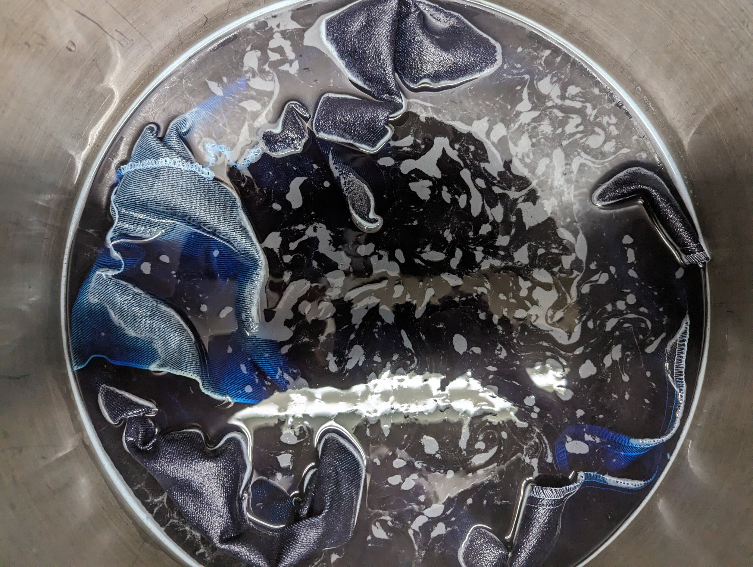 A stainless steel sink with black and blue elastic fabric strips soaked in soapy water.