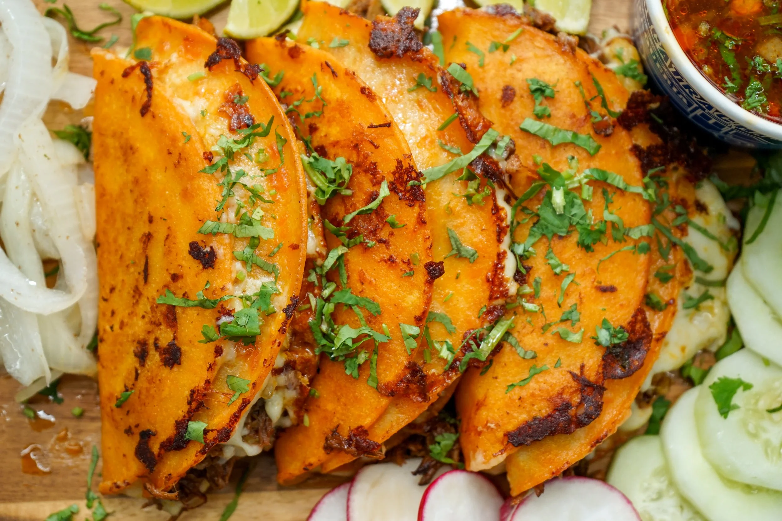 Close-up of grilled Mexican street corn coated in chili powder and garnished with chopped cilantro, served on a wooden platter with sliced radishes, cucumbers, and lime wedges.