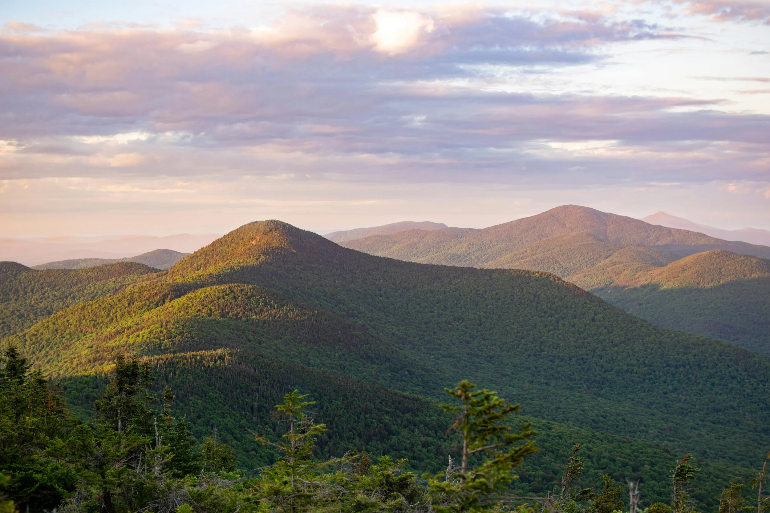 A scenic view of green mountain ranges under a partly cloudy sky during sunset.