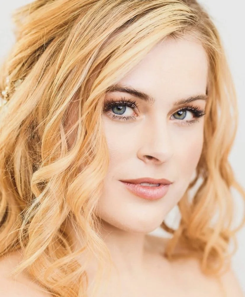 Close-up of a woman with wavy blonde hair and blue eyes.