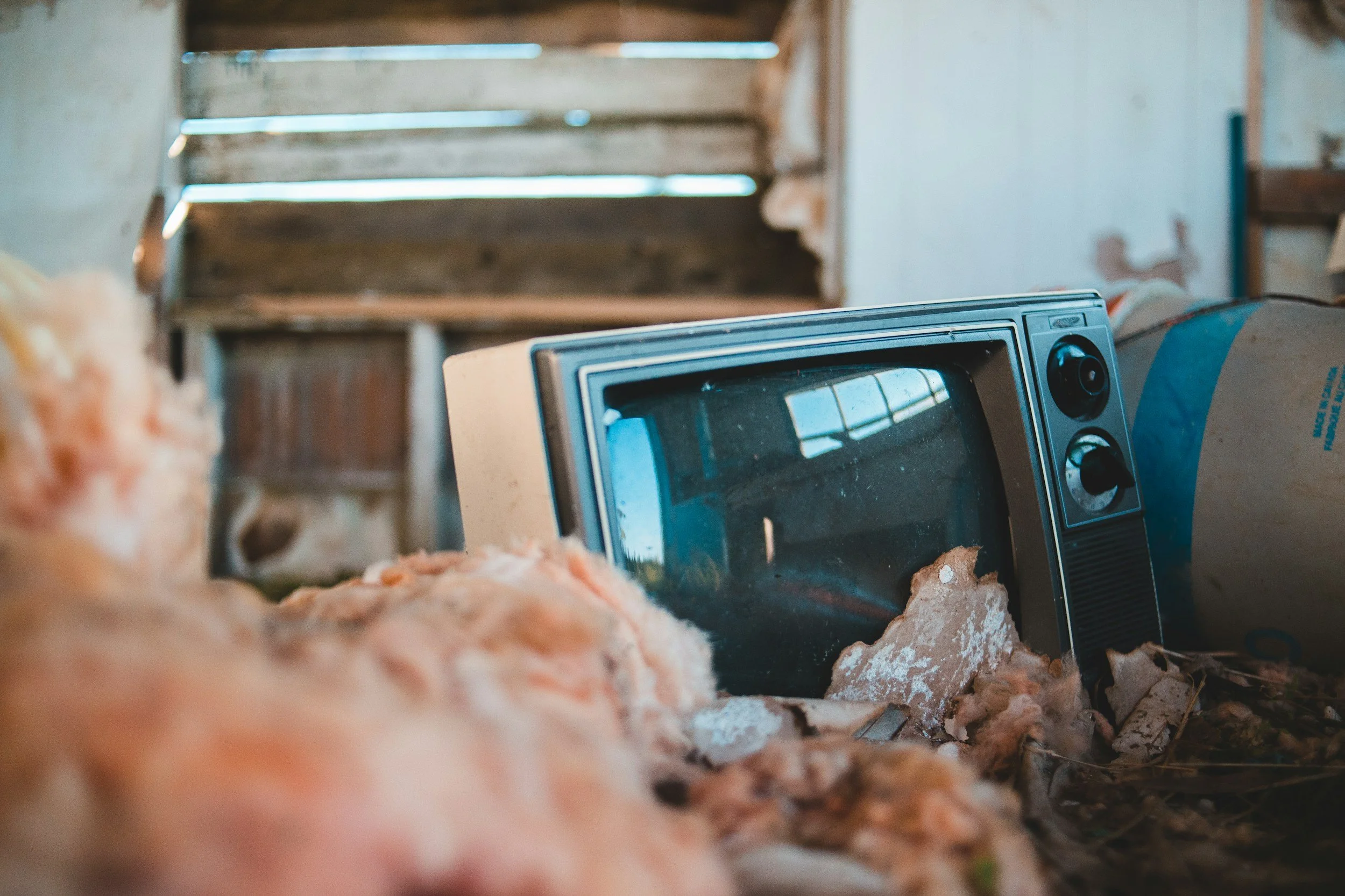 An old microwave oven in a cluttered, rustic setting with wooden shelves and uneven plaster walls, appearing to be in a barn or shed.