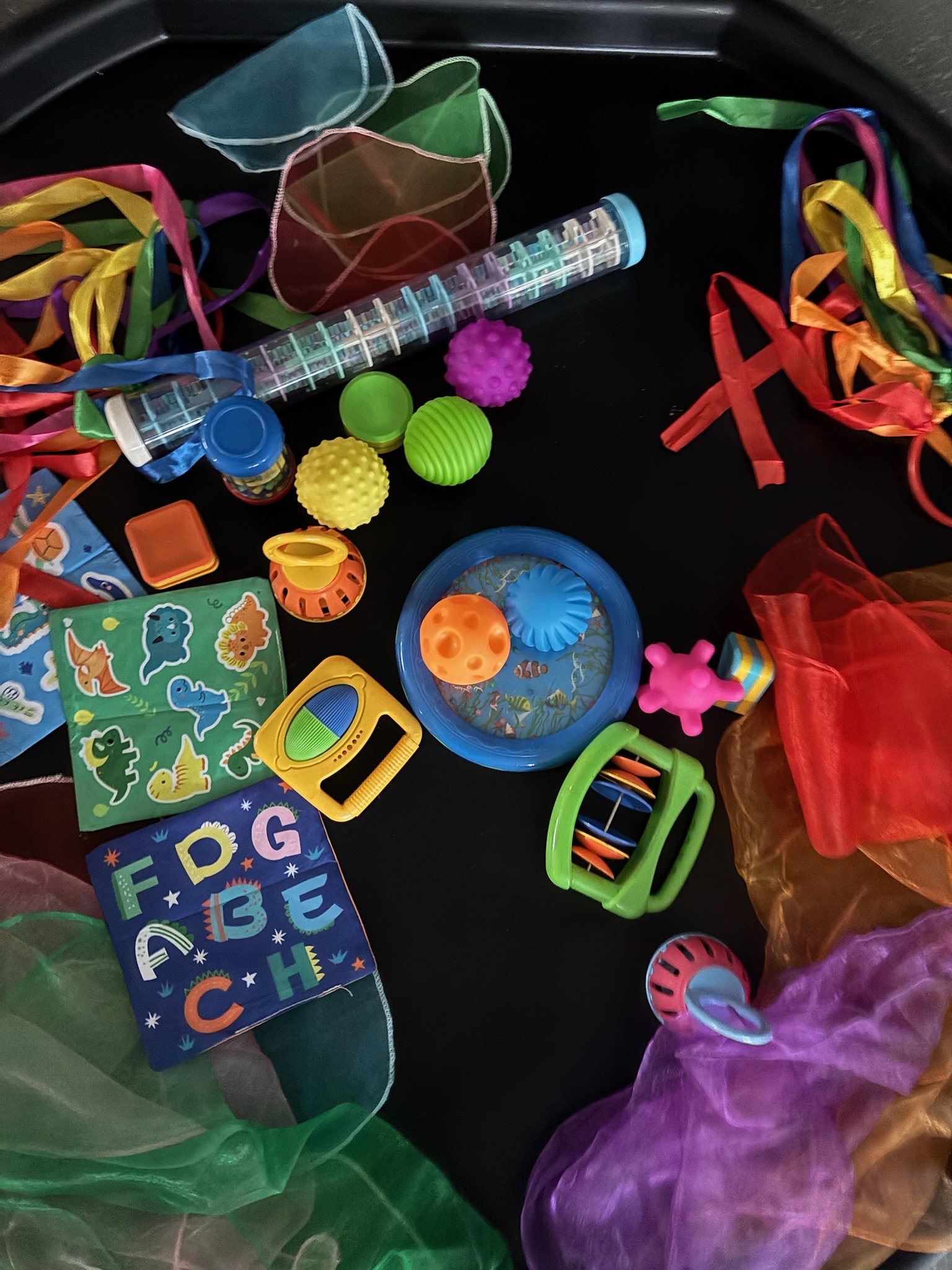 Colorful plastic toys, ribbons, balls, and books inside a storage bin.