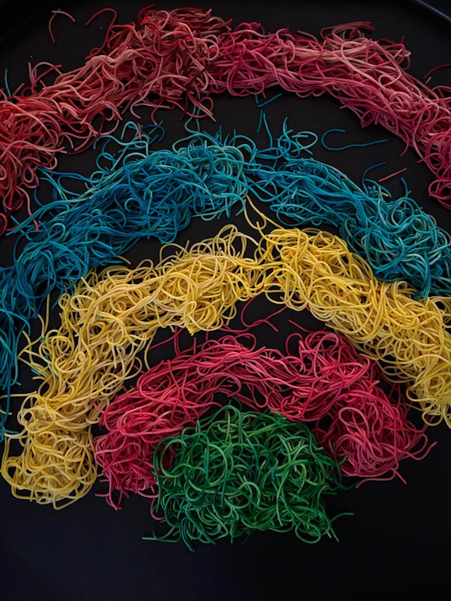 Colorful rubber bands arranged in the shape of a rainbow on a black surface.