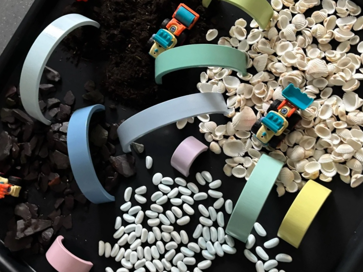 Colorful toy blocks and seashells in a container, with some scattered white oval-shaped pills and dark rocks.