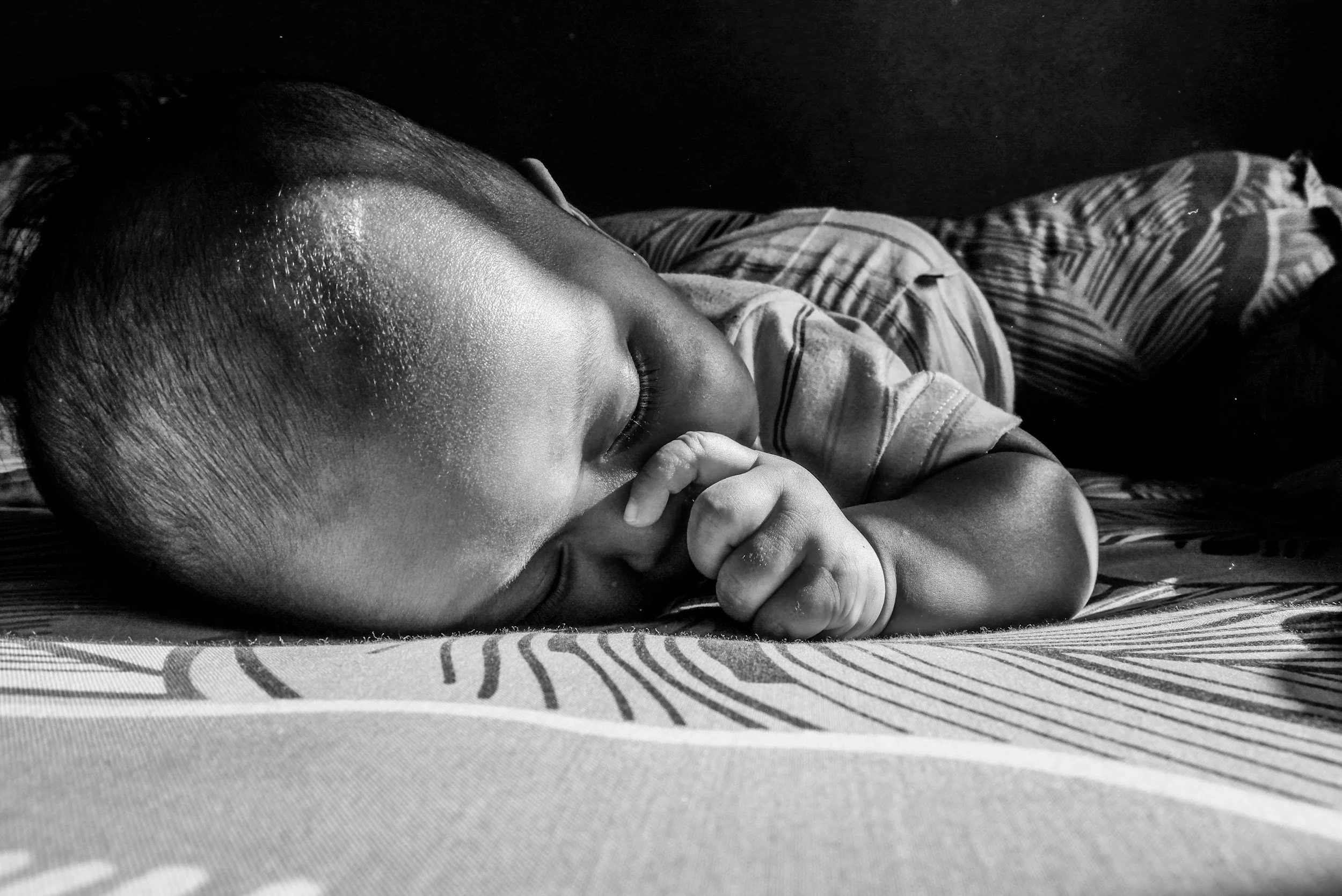 A young child, sleeping peacefully with eyes closed, lying on a bed with striped sheets.