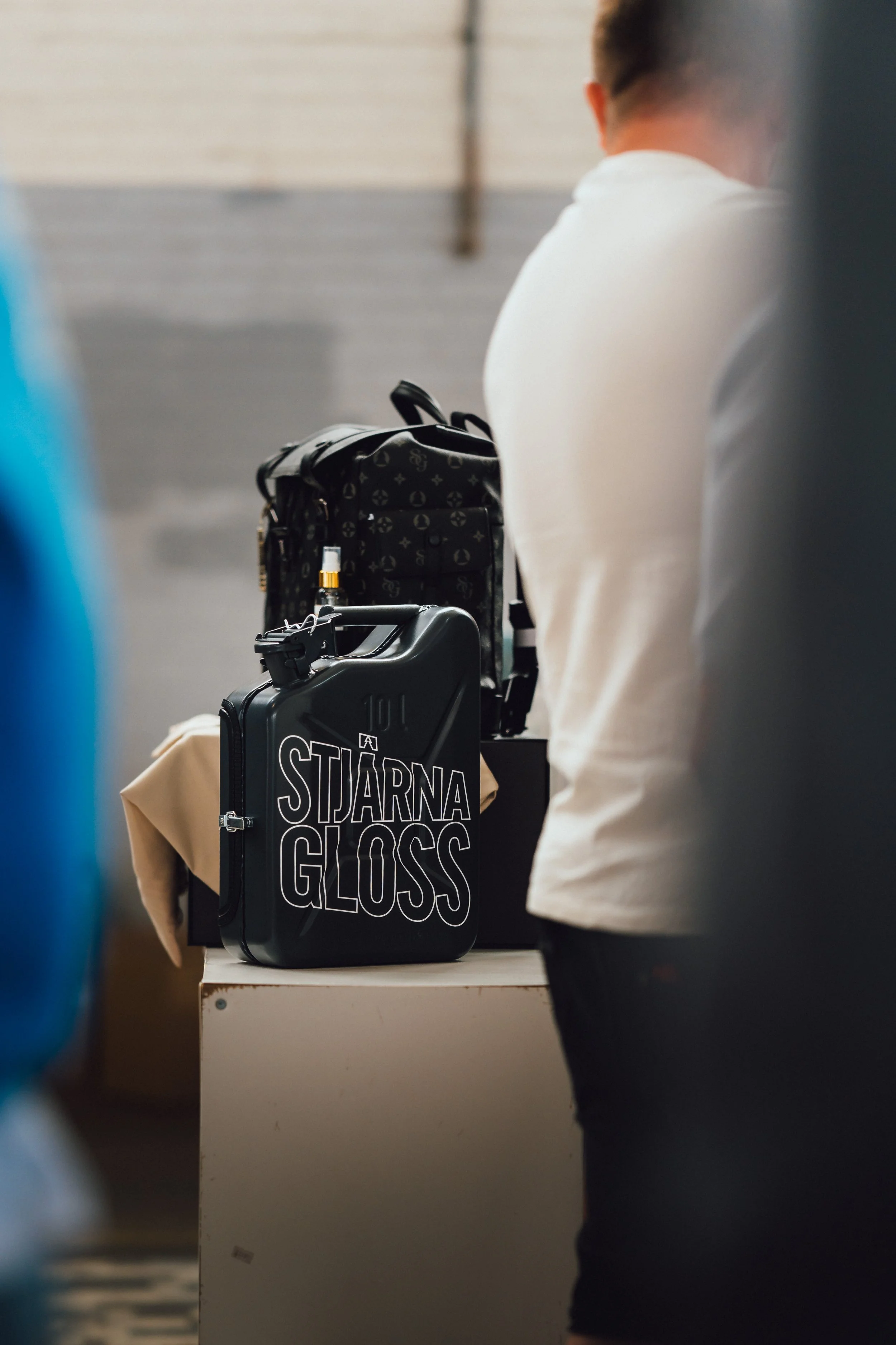 A person standing at a counter with luggage and a bag that has the words 'STÄRNA GLOSS' on it, in an indoor setting.