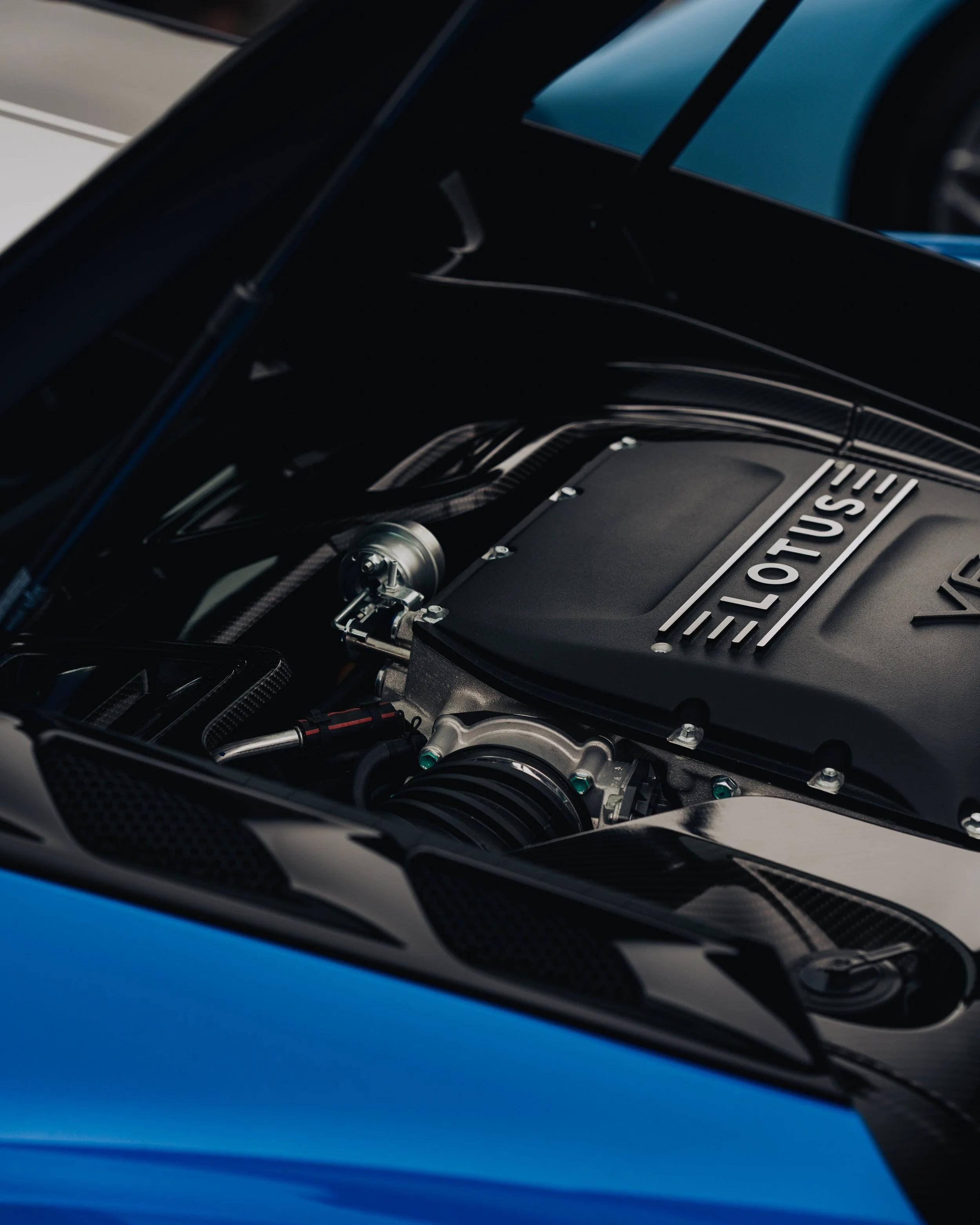 Close-up of a blue car engine bay and part of the hood with a silver 'LOTUS' badge visible.