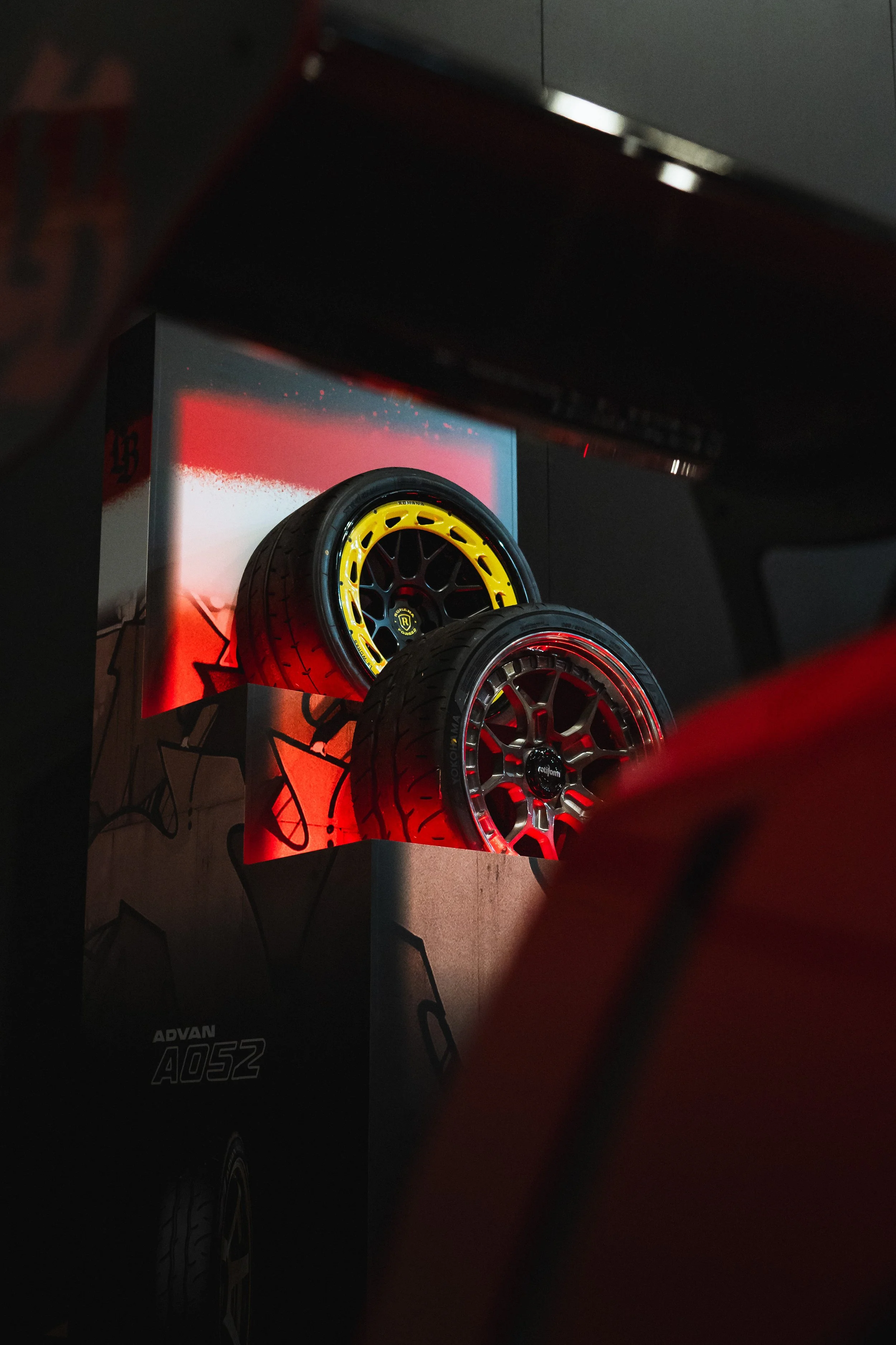Close-up of black and yellow racing wheels displayed on a stand with red lighting at an automotive event.