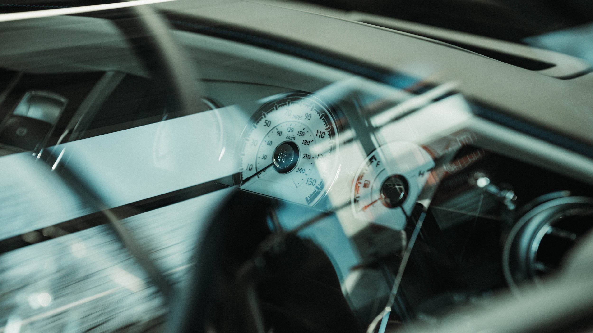 Close-up view of a car's speedometer and dashboard, with a reflection on the windshield.