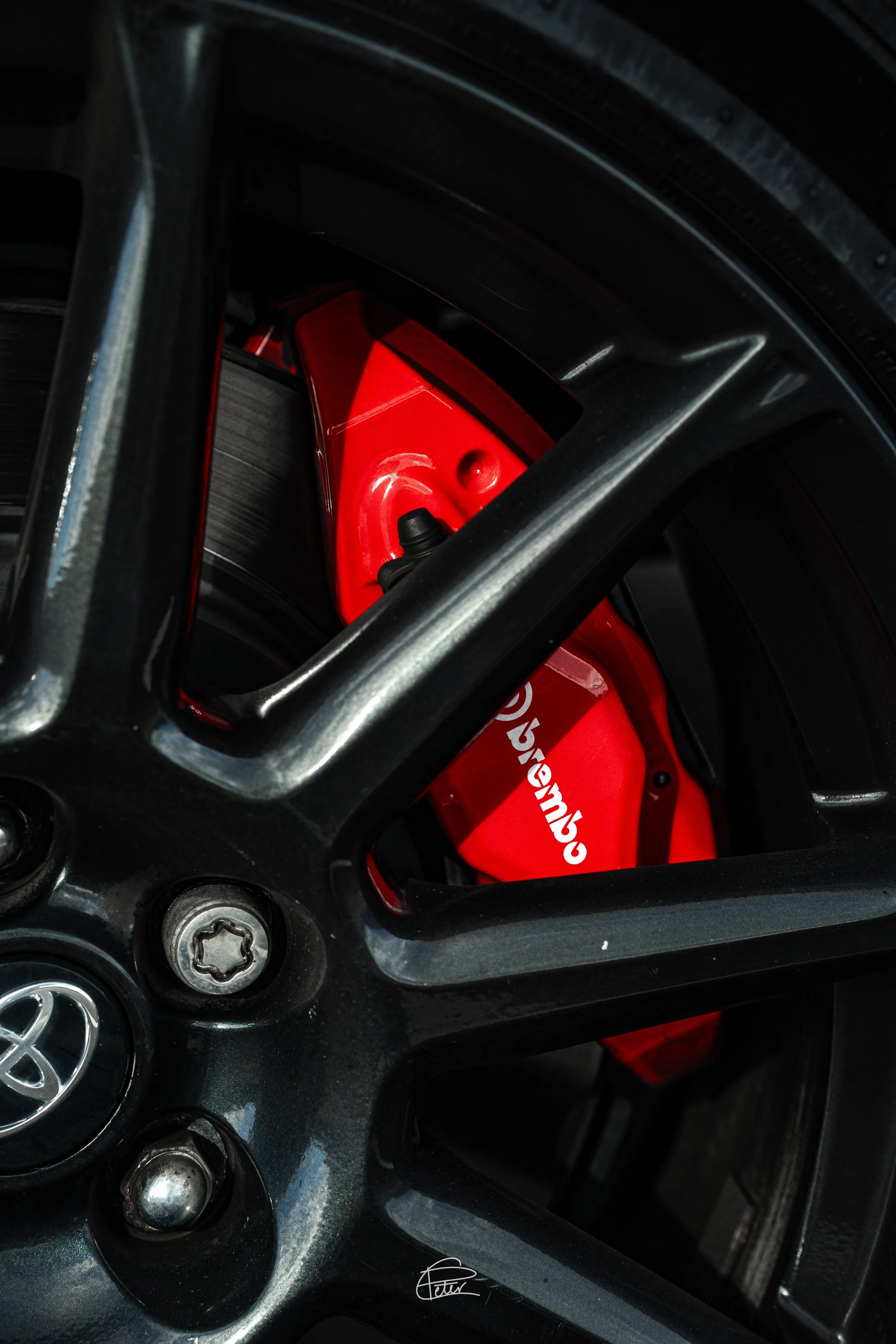 Close-up of a black car wheel with a visible brake caliper painted red and bearing the Ducati logo.