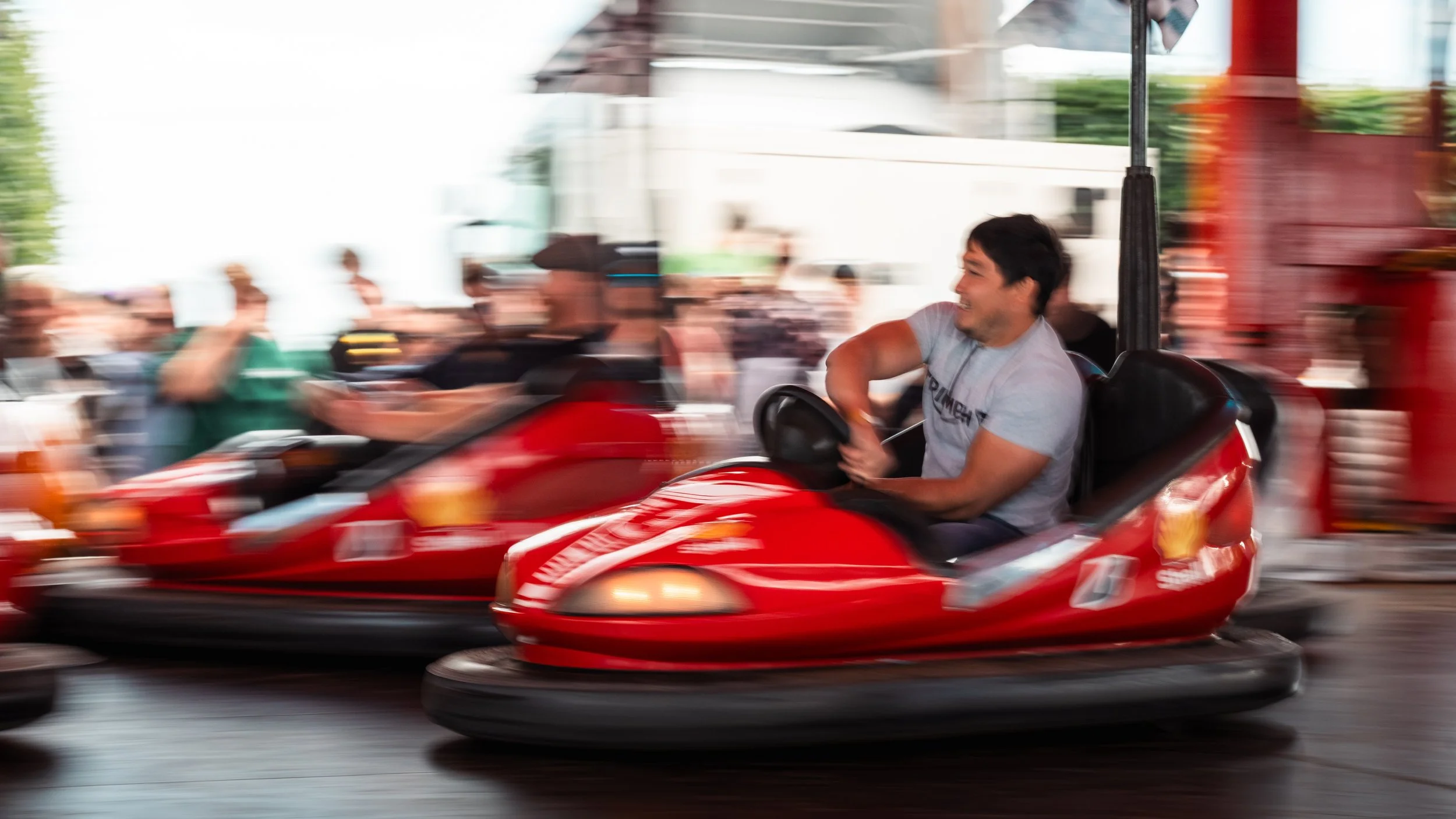 Young man smiling and riding a red go-kart on a busy street during daytime.