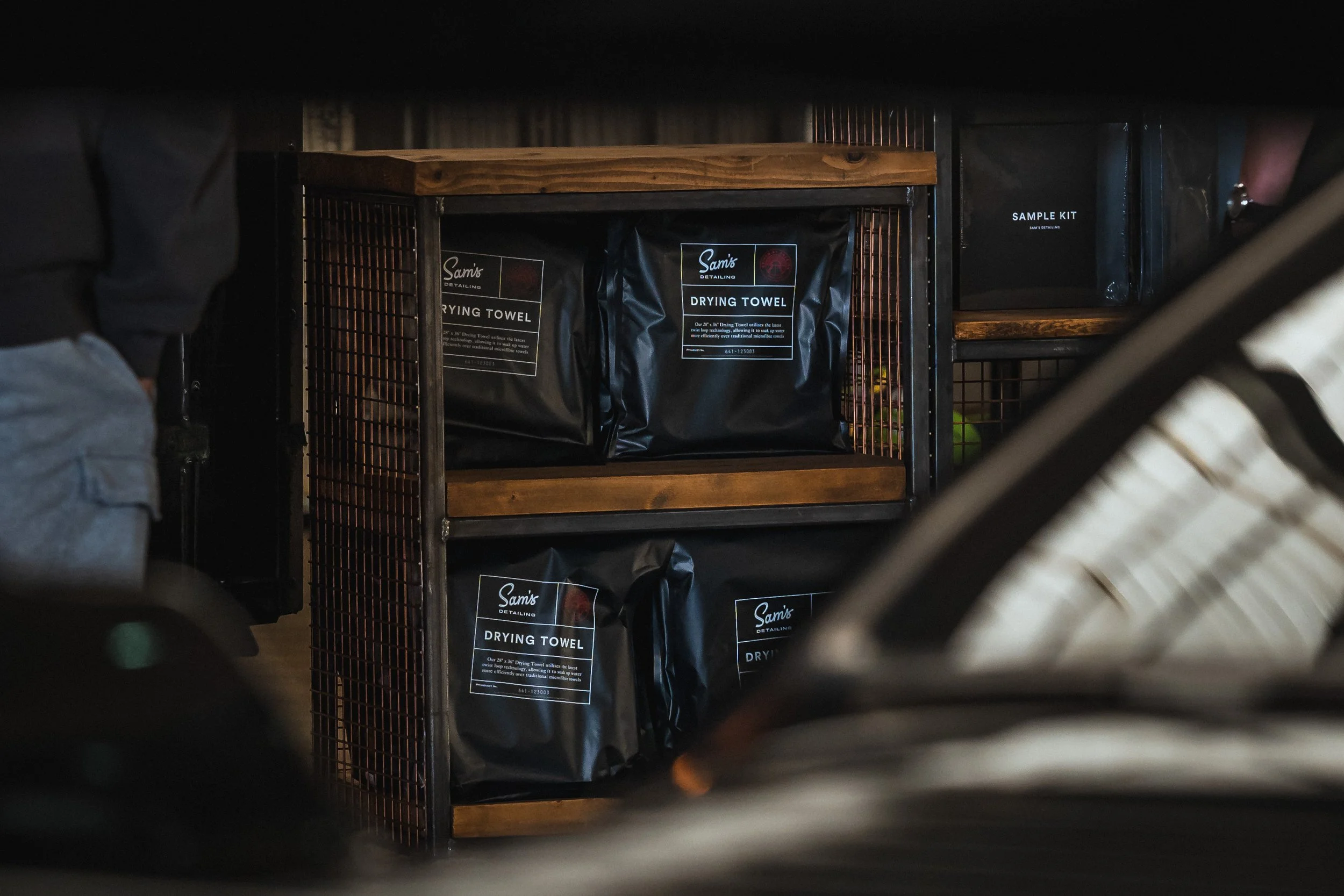 Shelves stocked with Sam's Detailing drying towels and sample kits, viewed through a small opening.