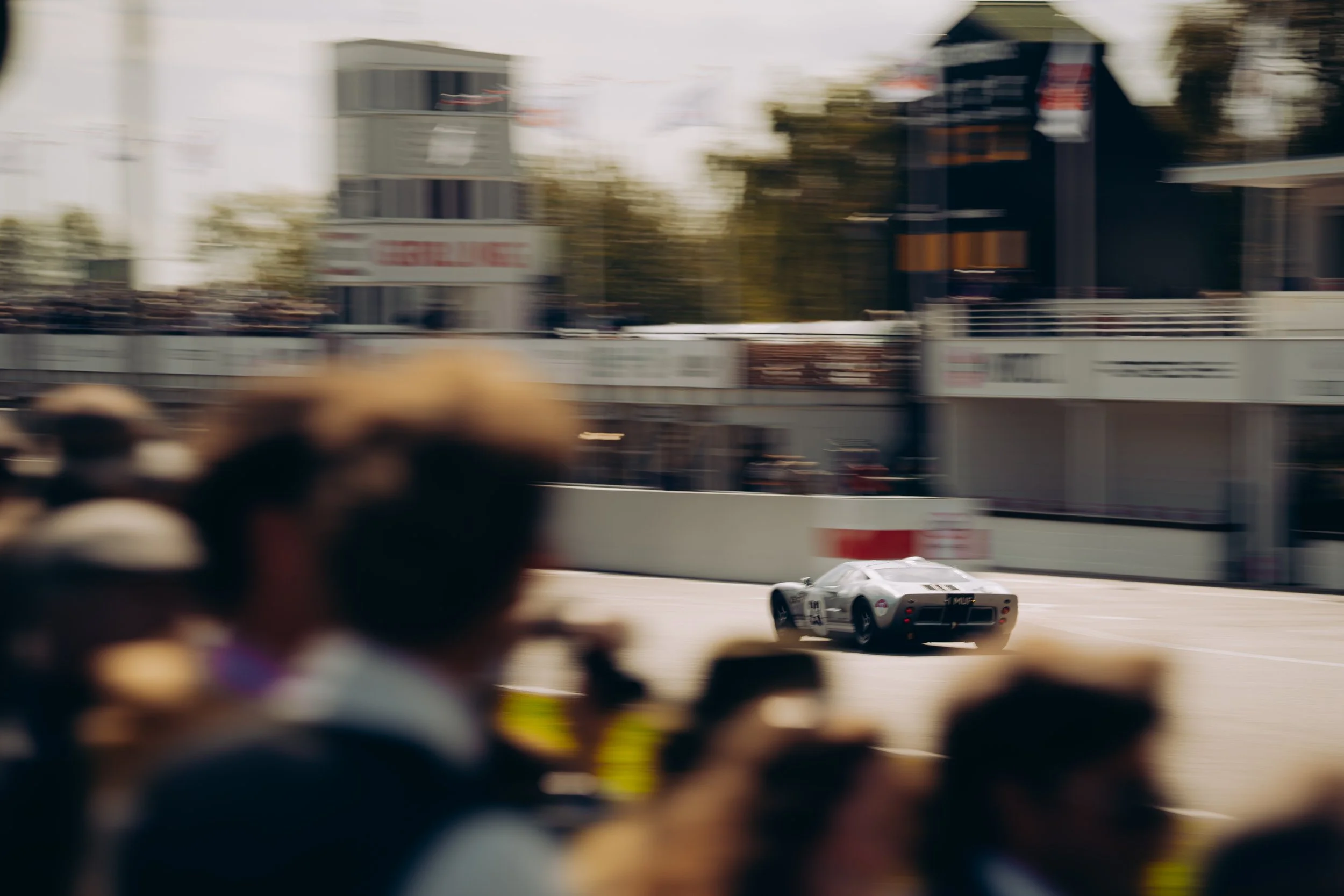 Race car on a racetrack with spectators and structures in the background, blurred motion shot.