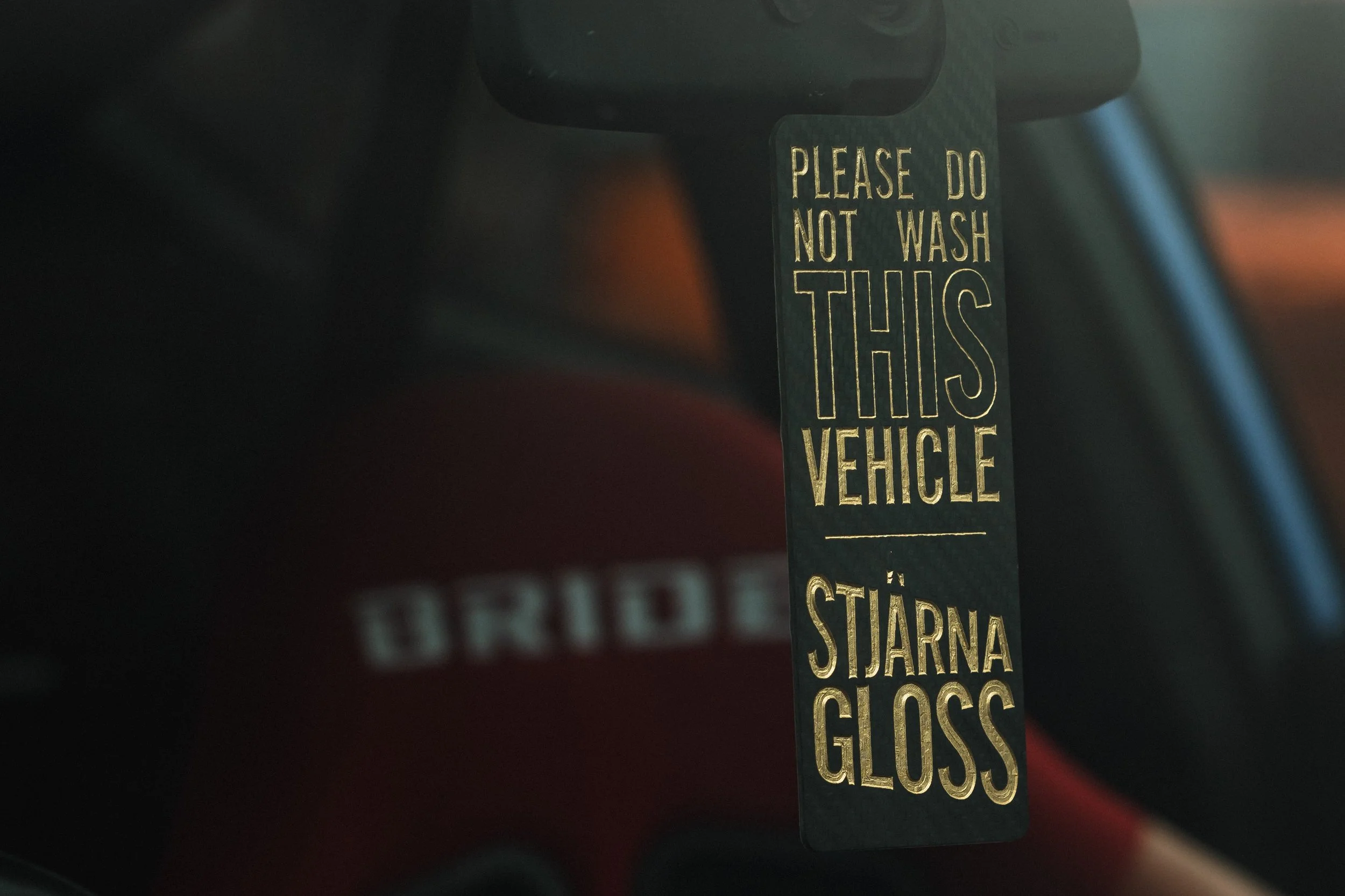 A parking permit hanging from a vehicle's rearview mirror with the text 'Please do not wash this vehicle' and instructions for a starlight glazing process.