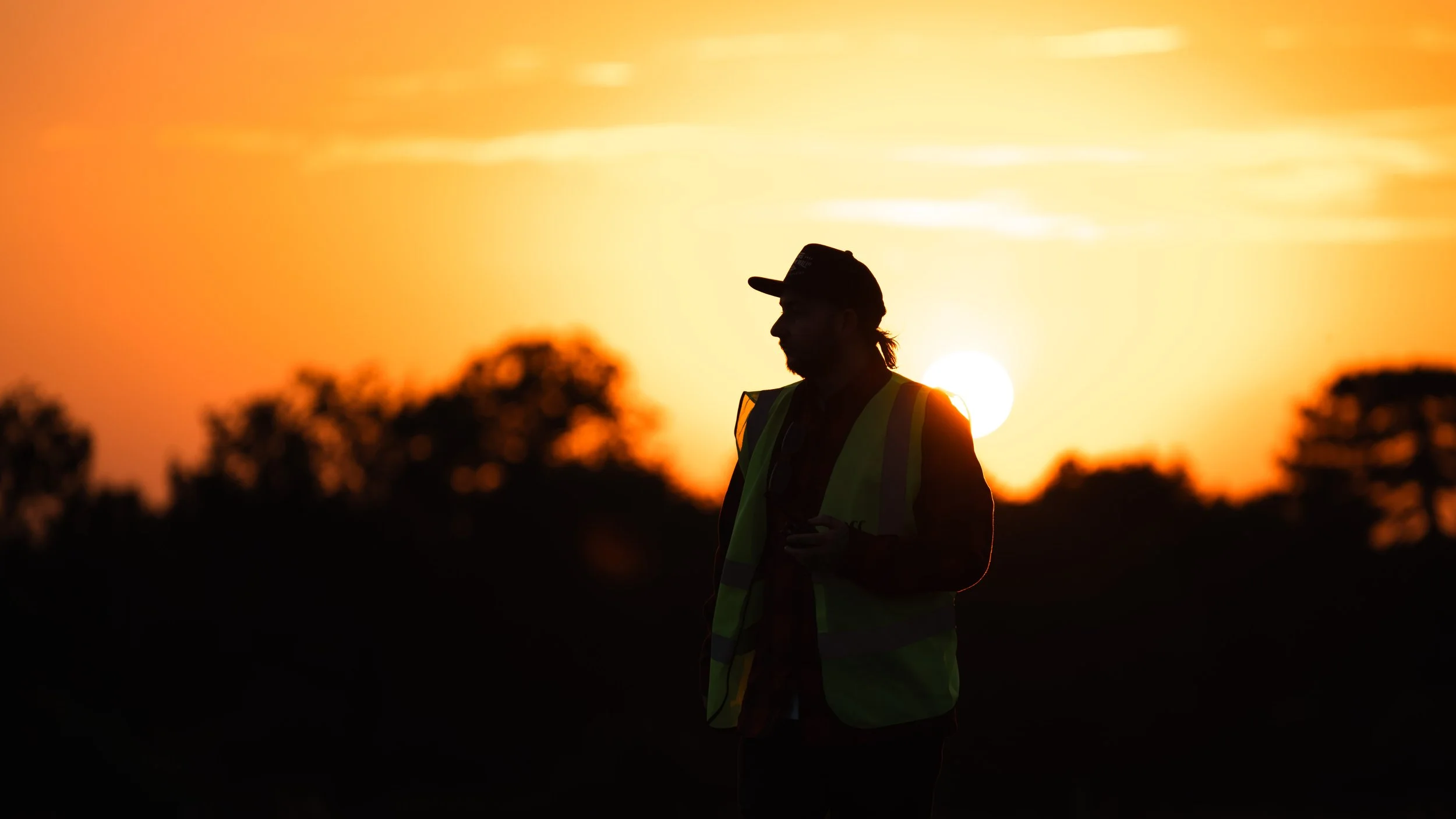 Silhouette of a person wearing a safety vest and cap during sunset.
