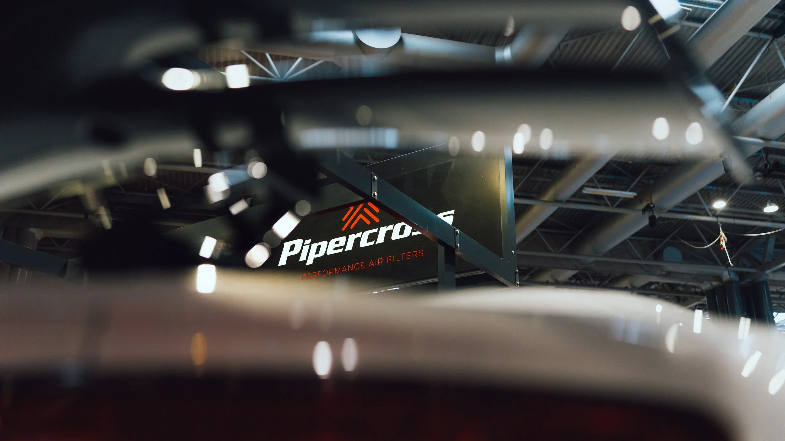 View through a gap showing a sign for PiperCross performance air filters with an industrial ceiling in the background.