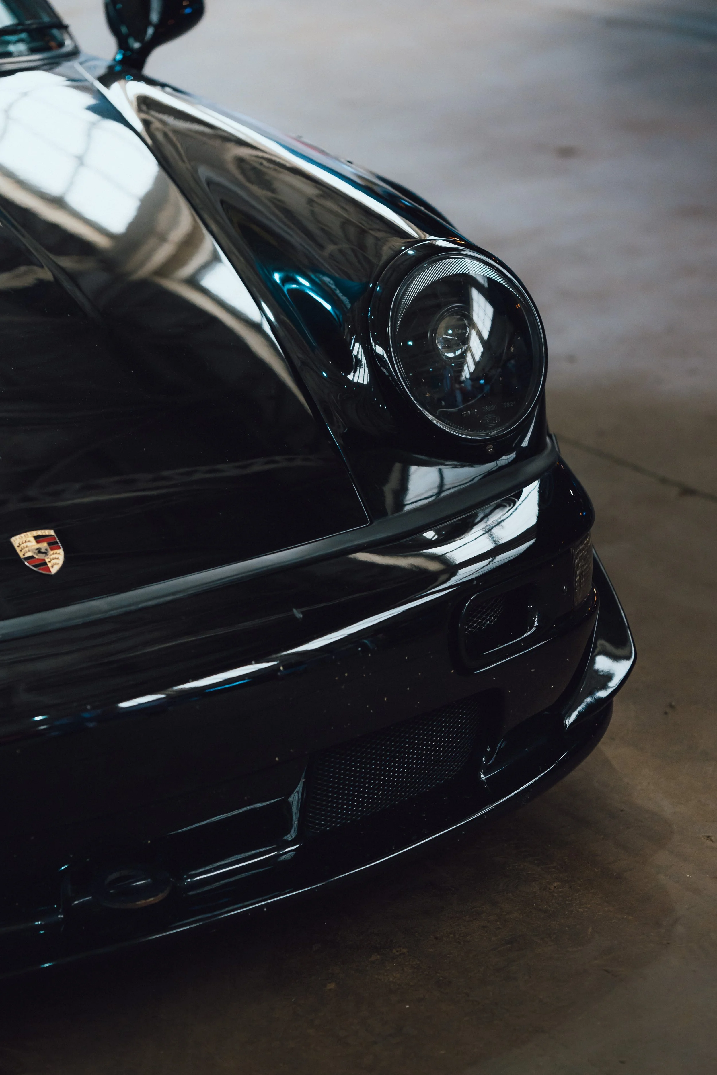 Close-up of the front part of a black Porsche sports car, showing the headlight and part of the front bumper.