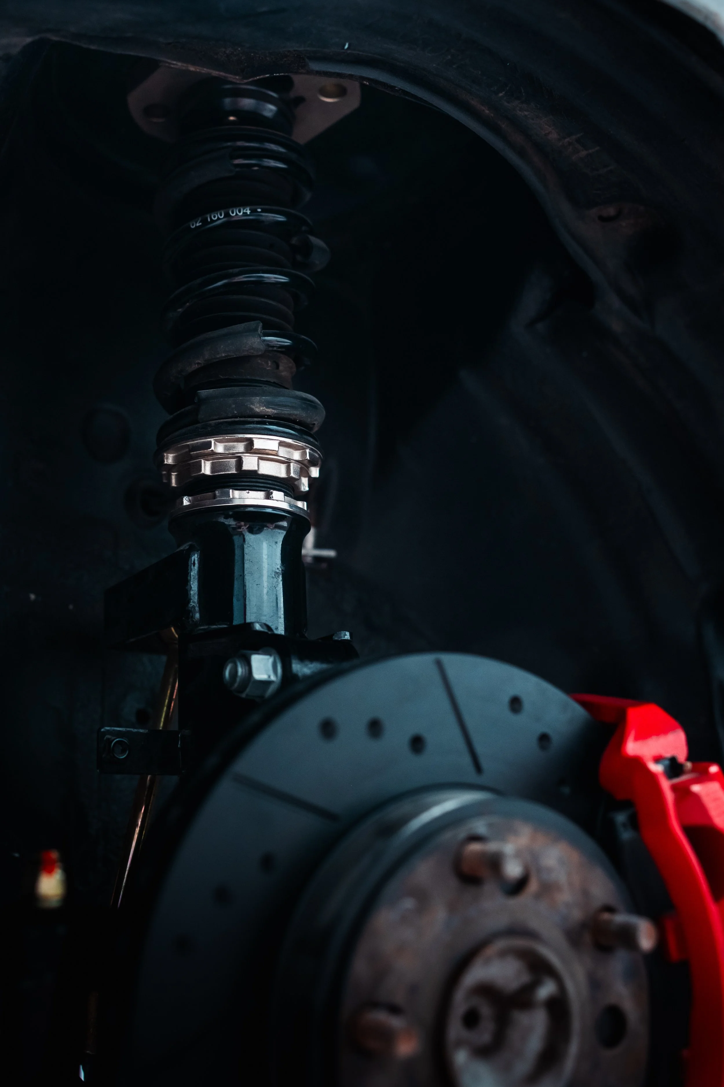 Close-up view of a car's suspension system, showing a coil spring and a part of the brake rotor with a red safety clip attached.