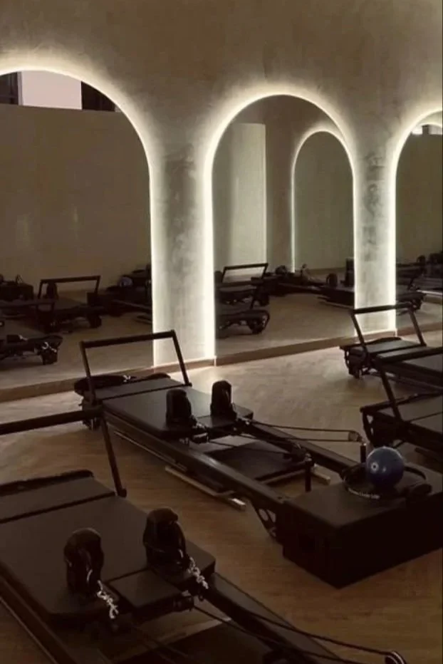 Pilates reformer machines in a dimly lit studio with arched wall cutouts and soft lighting.