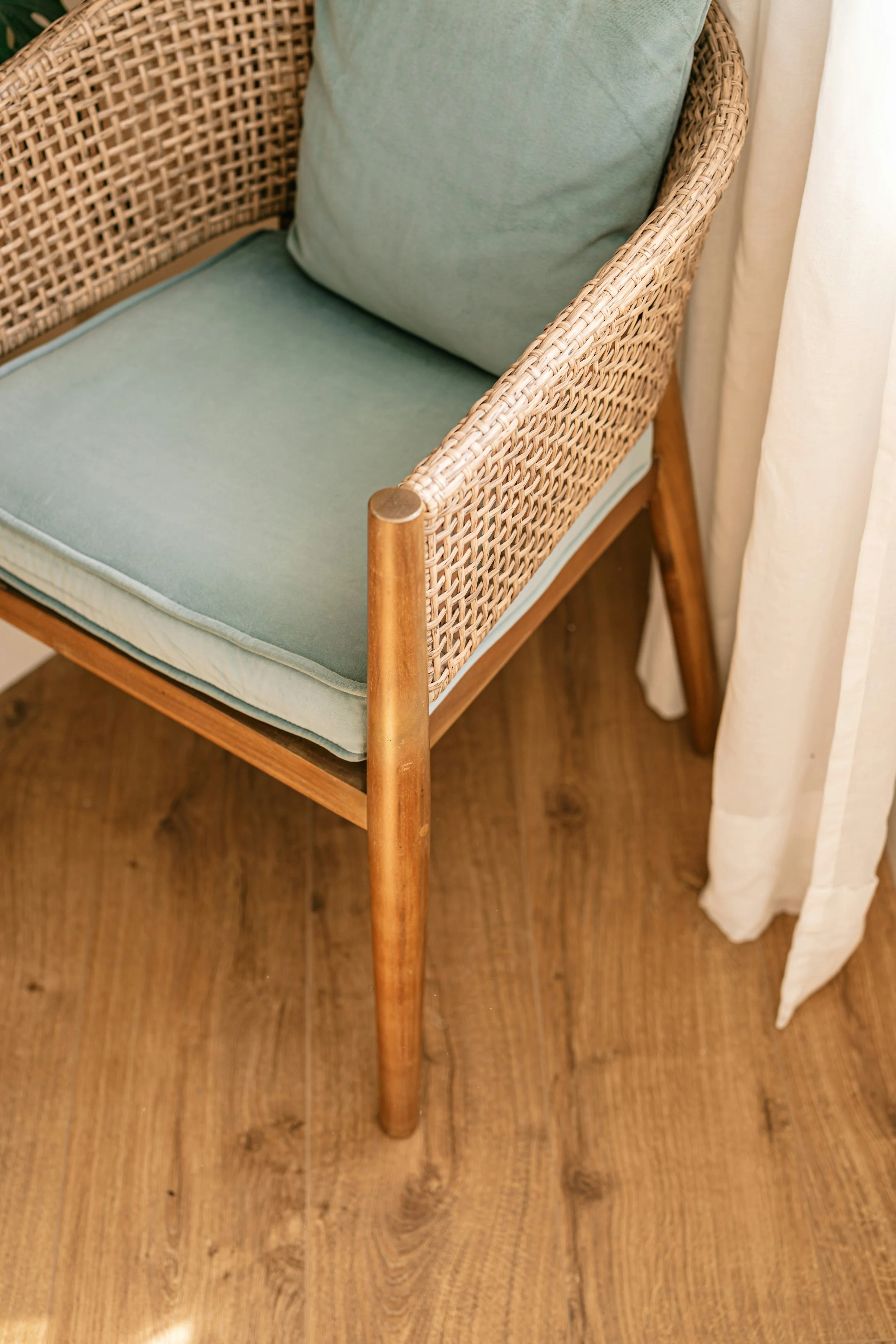 A wooden chair with a woven rattan backrest and light green cushions, positioned near a white curtain and a wooden floor for naturopathic doctor brand