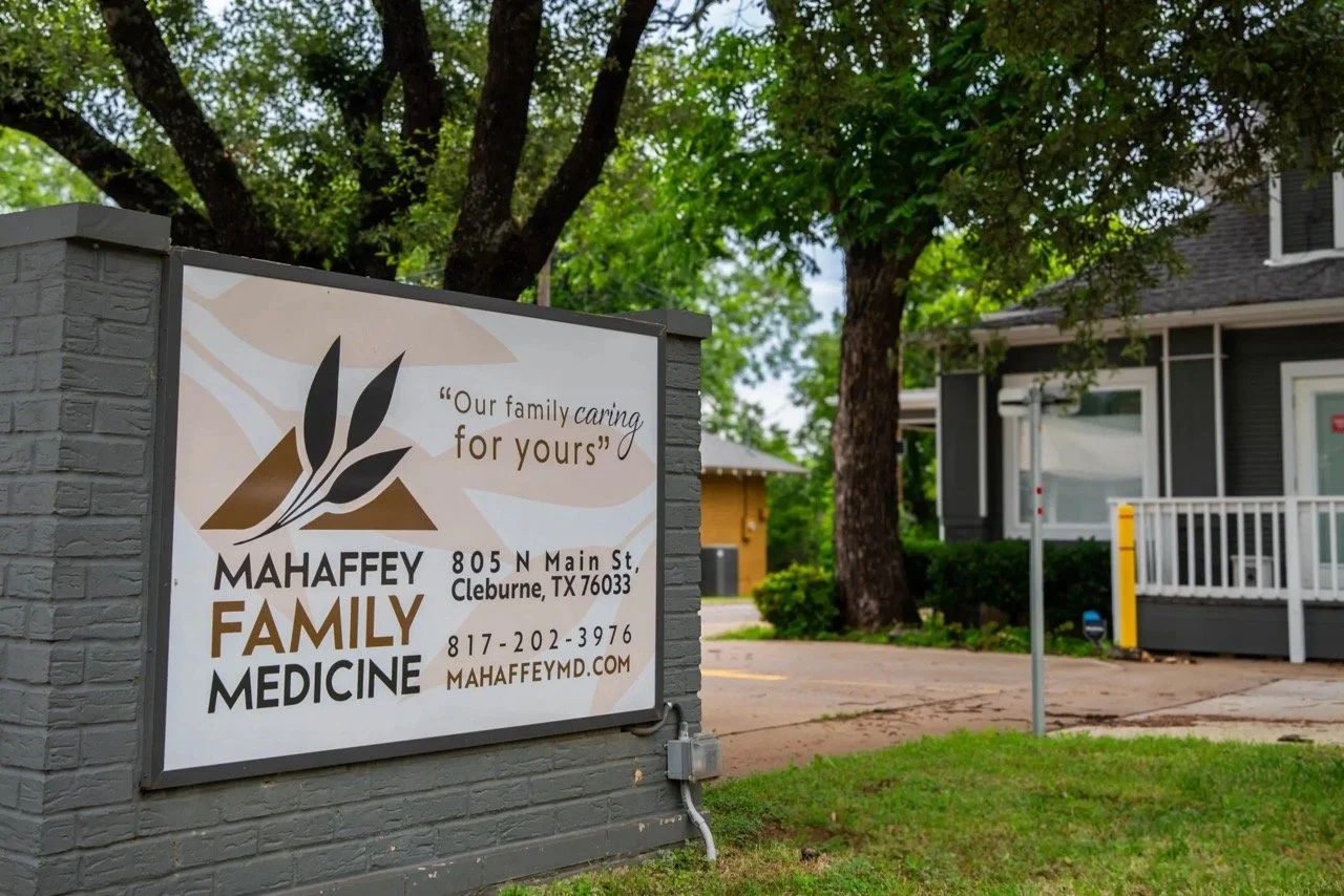Sign for Mahaffey Family Medicine with contact information, located at 805 N Main St, Cleburne, TX, surrounded by green trees and residential buildings in the background.