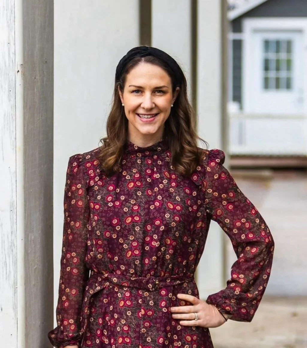 A woman with brown hair wearing a dark floral dress and a black headband, smiling outdoors.