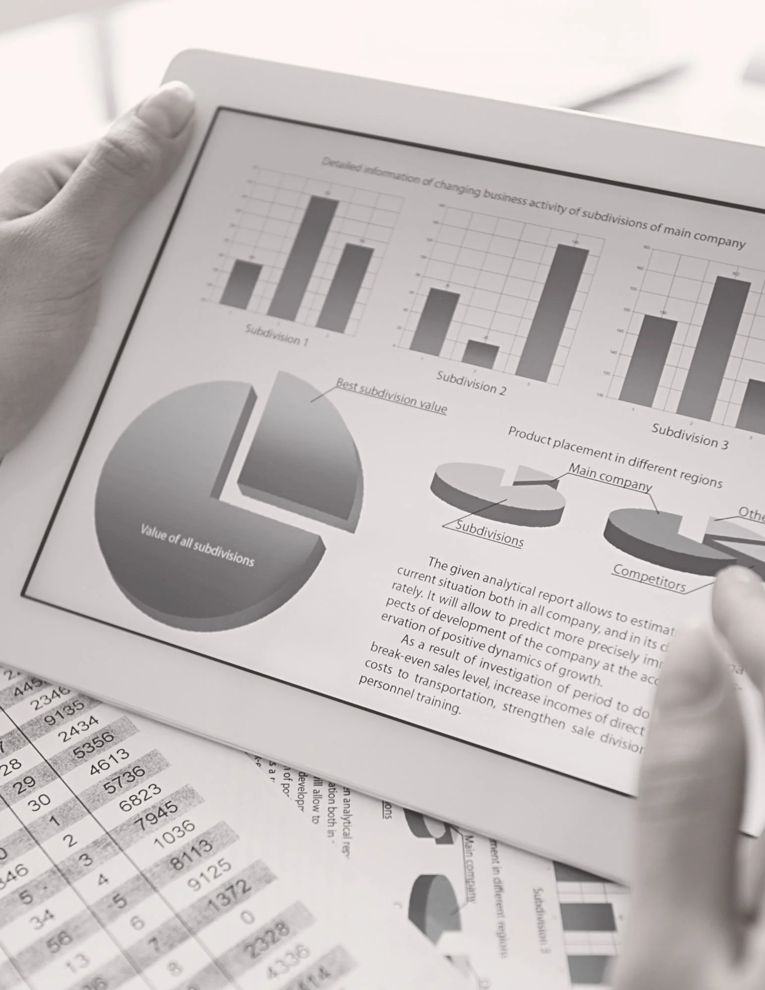 A person's hand holding a report with bar graphs and pie charts showing business activity and subdivision data, with financial spreadsheets and paper documents underneath.