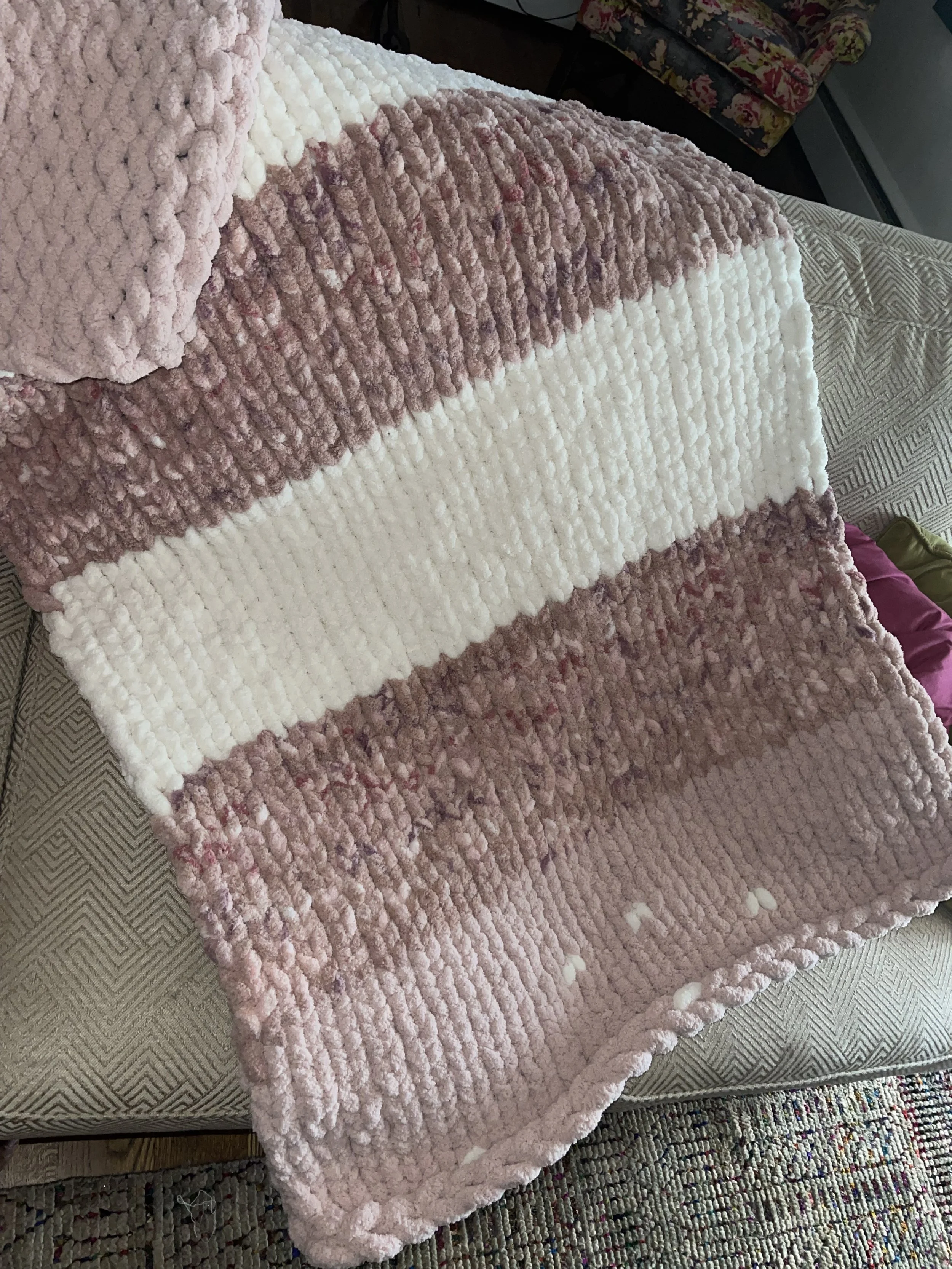 A cozy, plush blanket with pink, white, draped over a living room sofa.