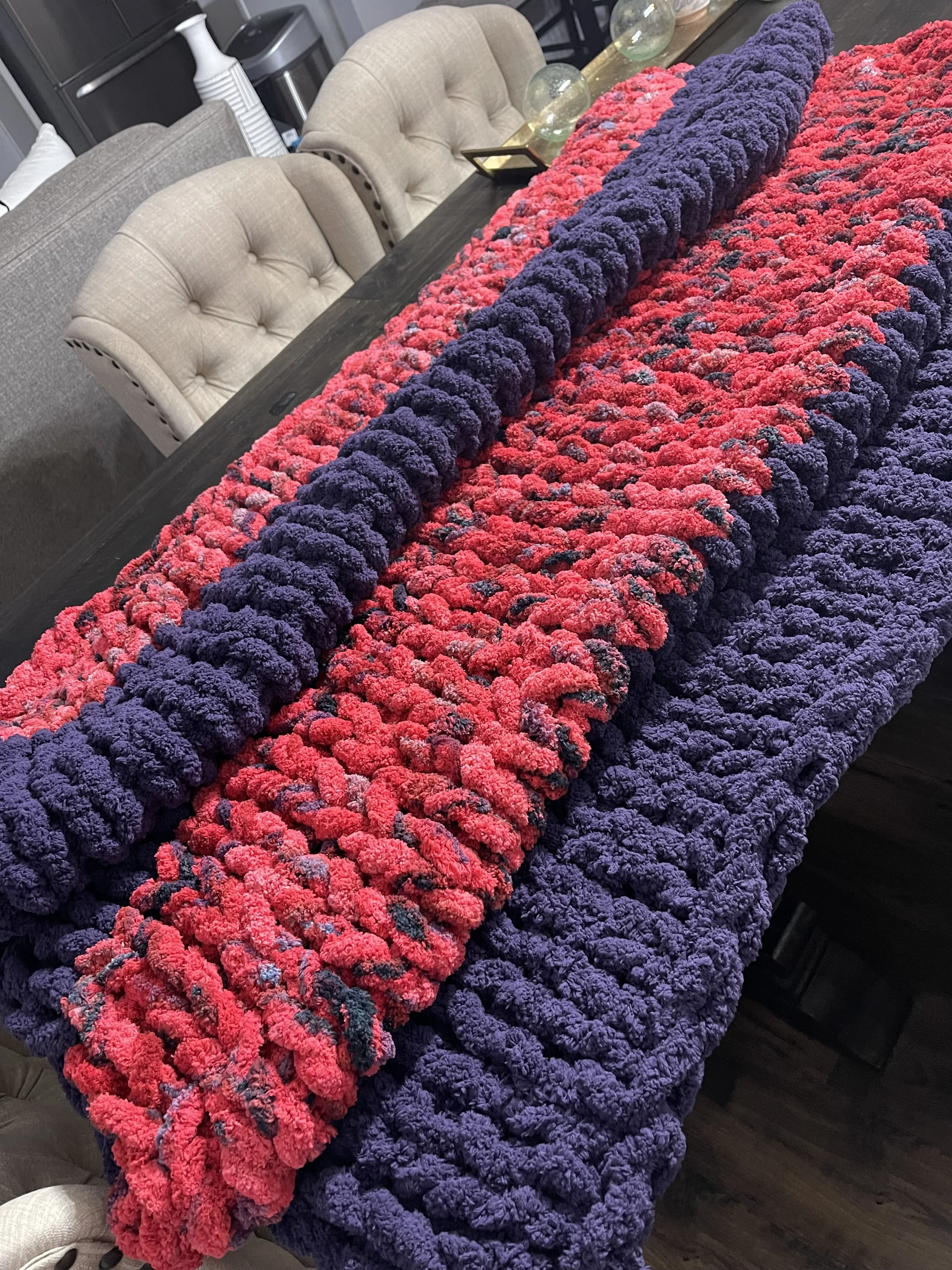 A colorful, textured crocheted blanket featuring purple and pink yarns.