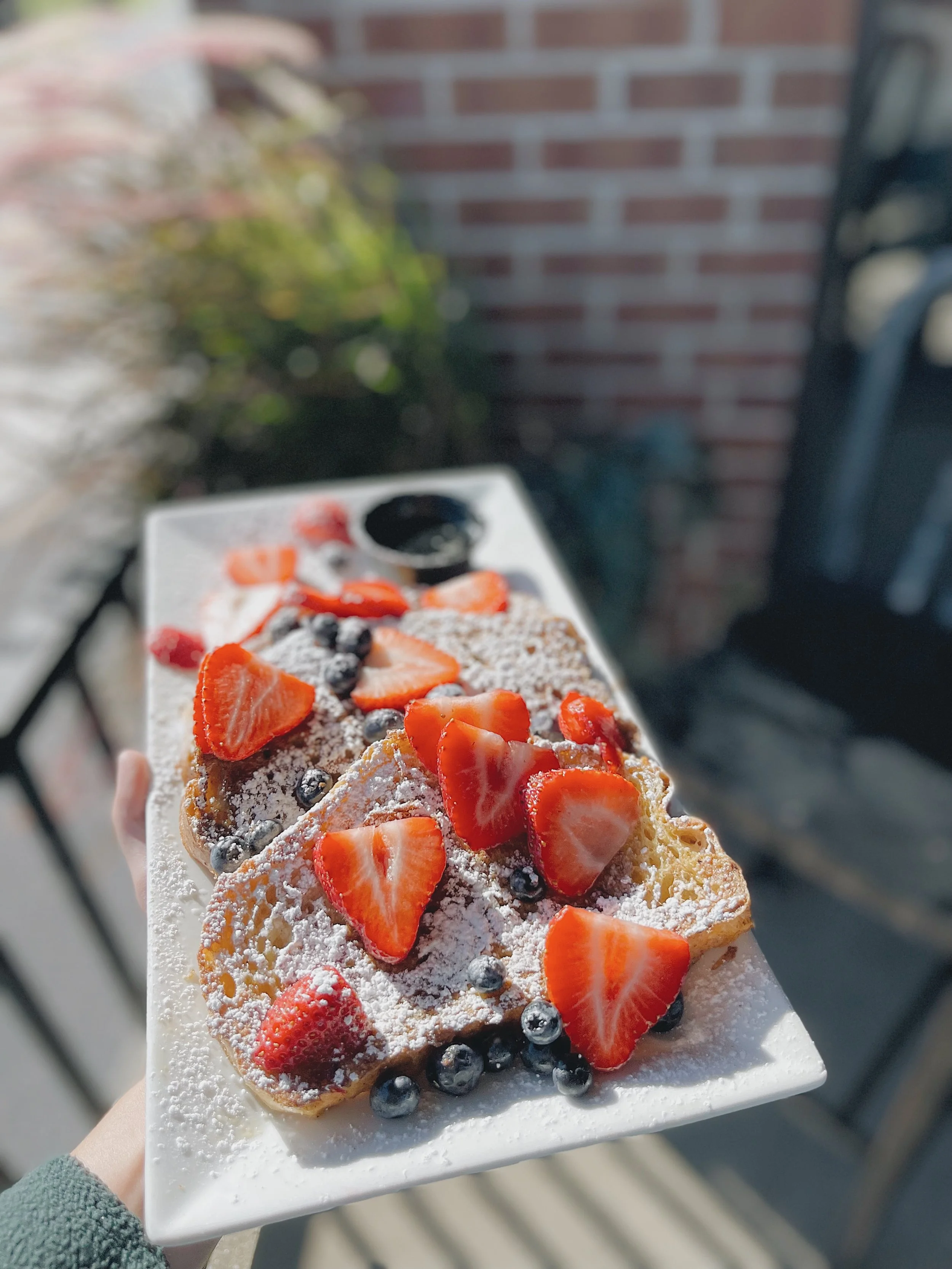A dessert topped with sliced strawberries, blueberries, and powdered sugar on a rectangular white plate.