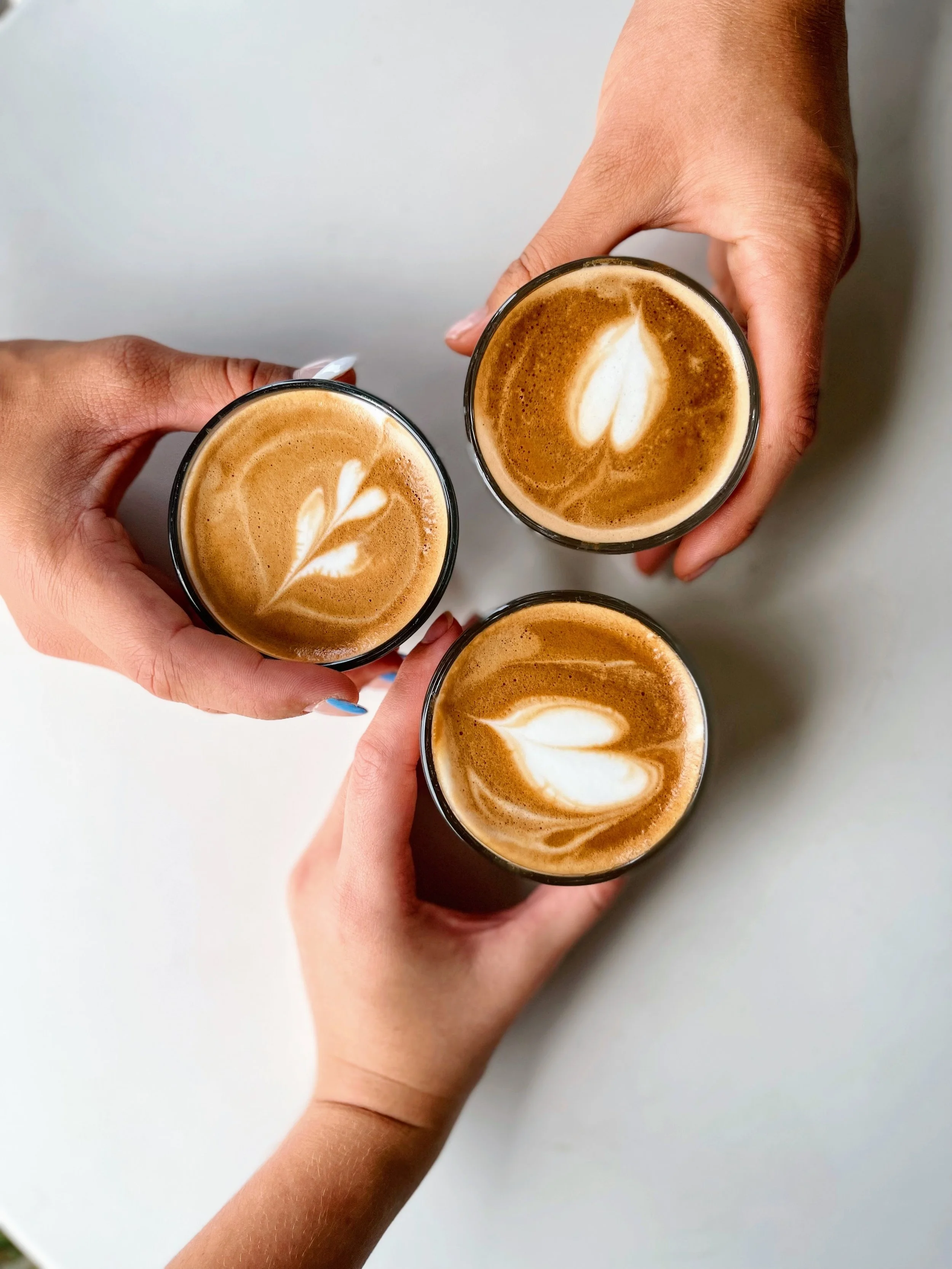 Multiple hands holding glasses of coffee with latte art, seen from above.