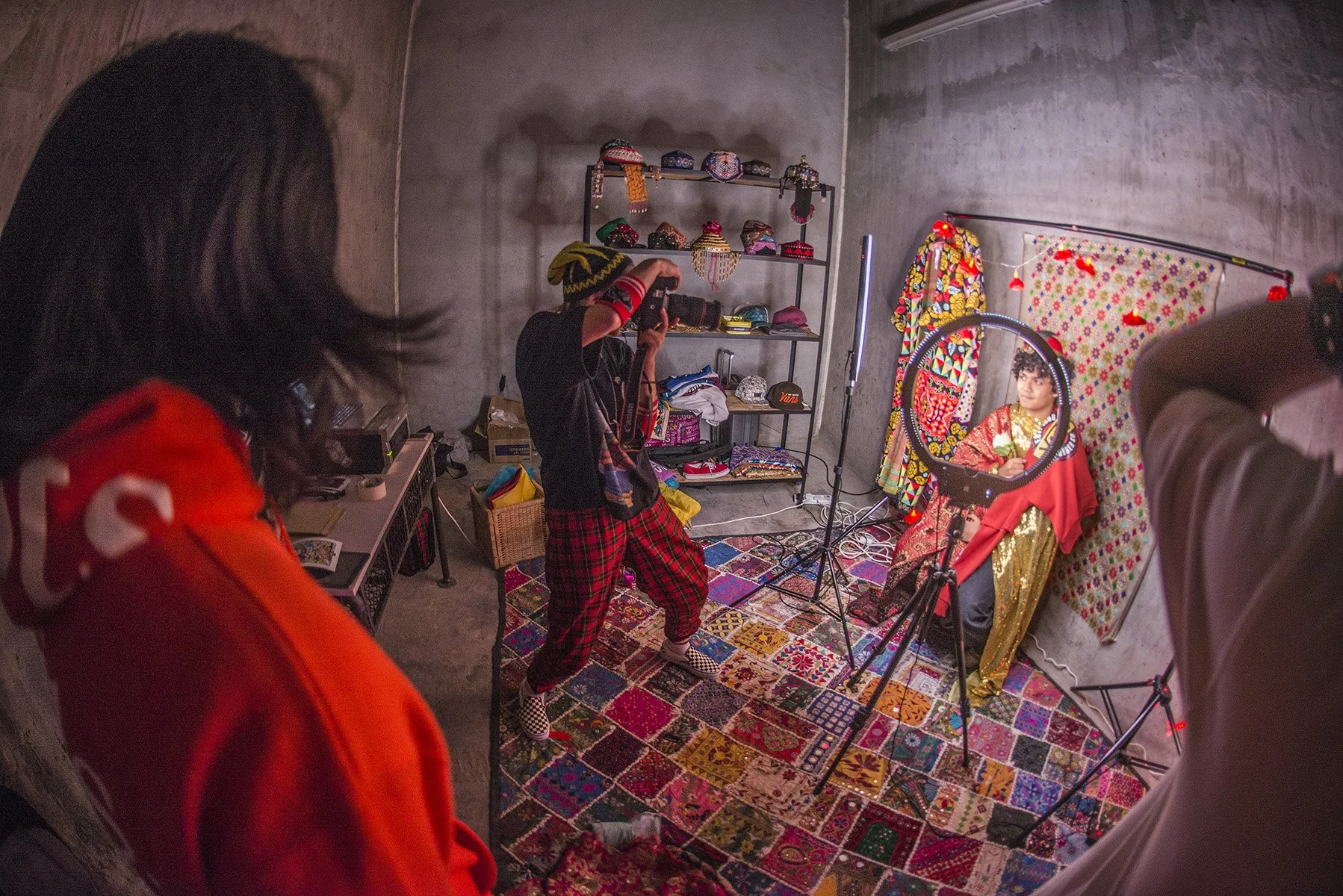 A photography session with a person dressed in vibrant traditional clothing in front of a colorful backdrop, surrounded by equipment and accessories, with a photographer taking pictures.