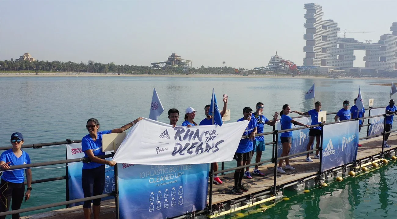 Group of people wearing blue shirts holding a banner on a dock by the water during a cleanup event.