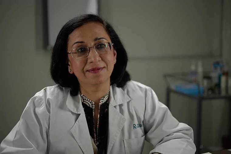 A woman in a white lab coat sitting in a medical or laboratory setting.