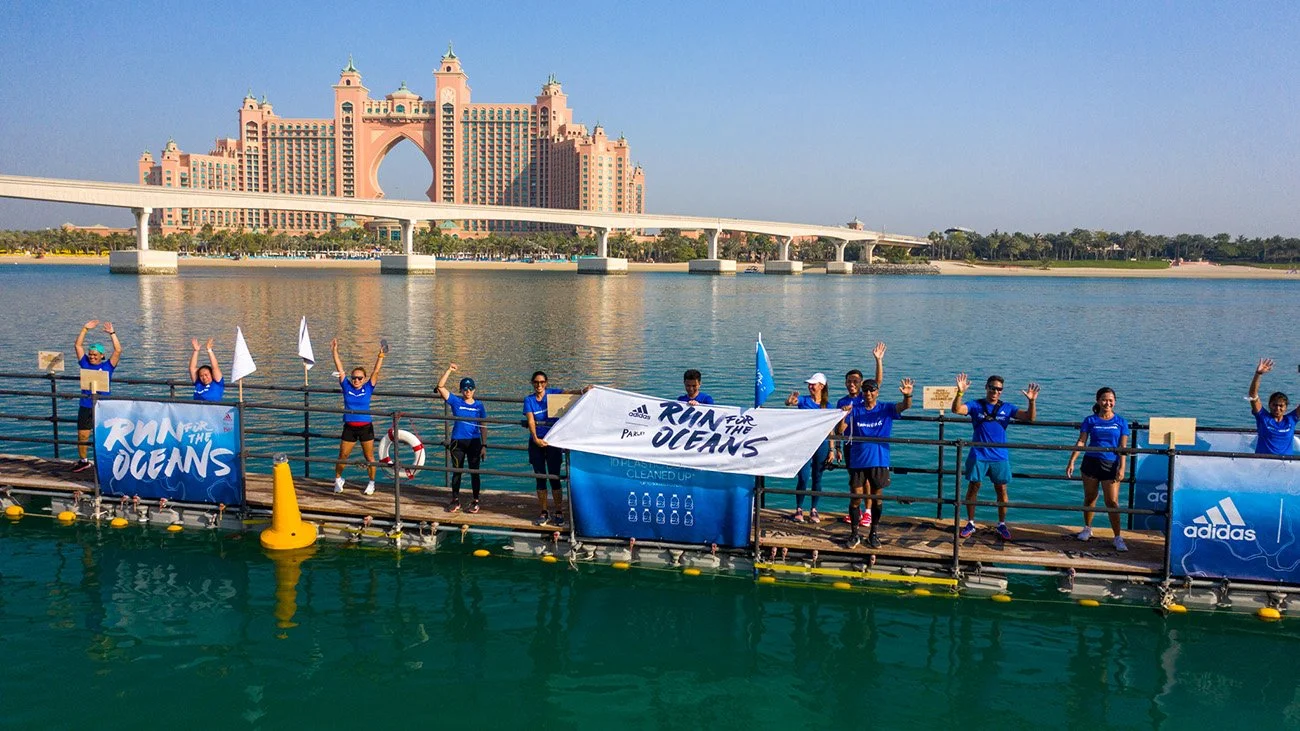 Group of people on a dock by the water, holding a banner that says 'Run for the Oceans' with the Dubai Atlantis Hotel in the background.