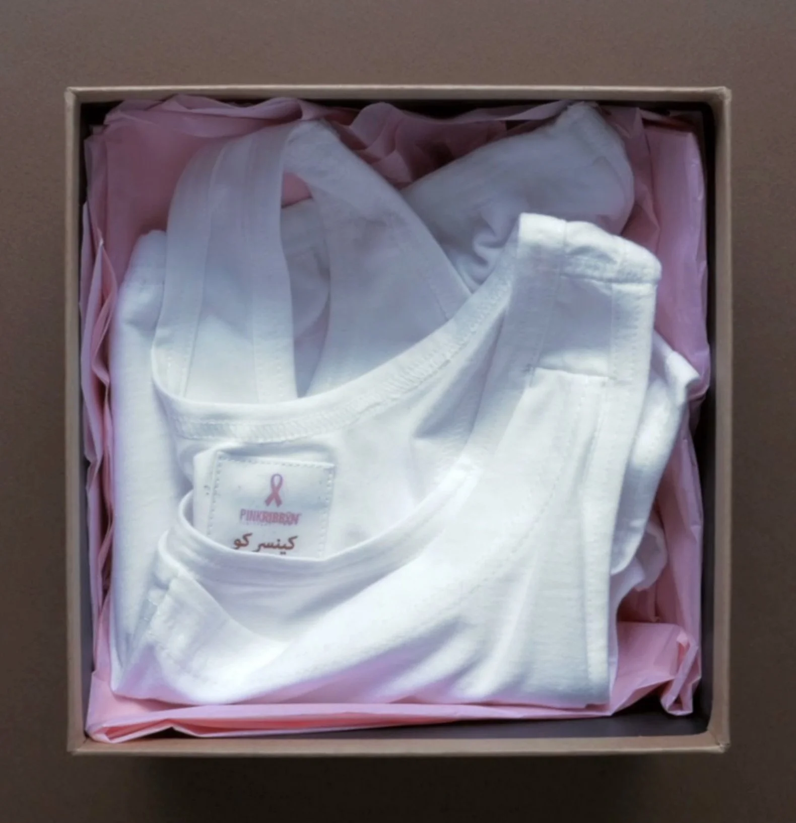 A box of folded white and pink bras inside a cardboard box with pink tissue paper lining.