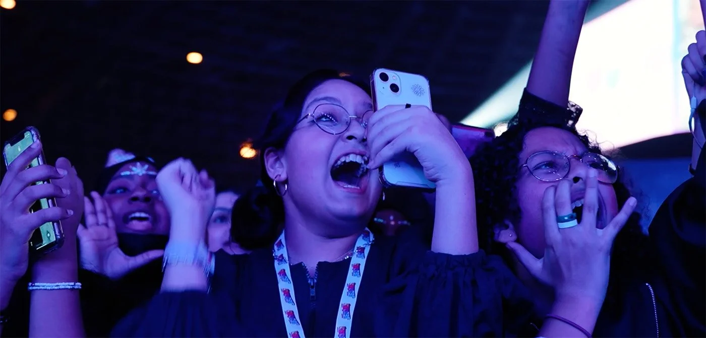 People excited and cheering at a concert or event, holding phones and making excited gestures.
